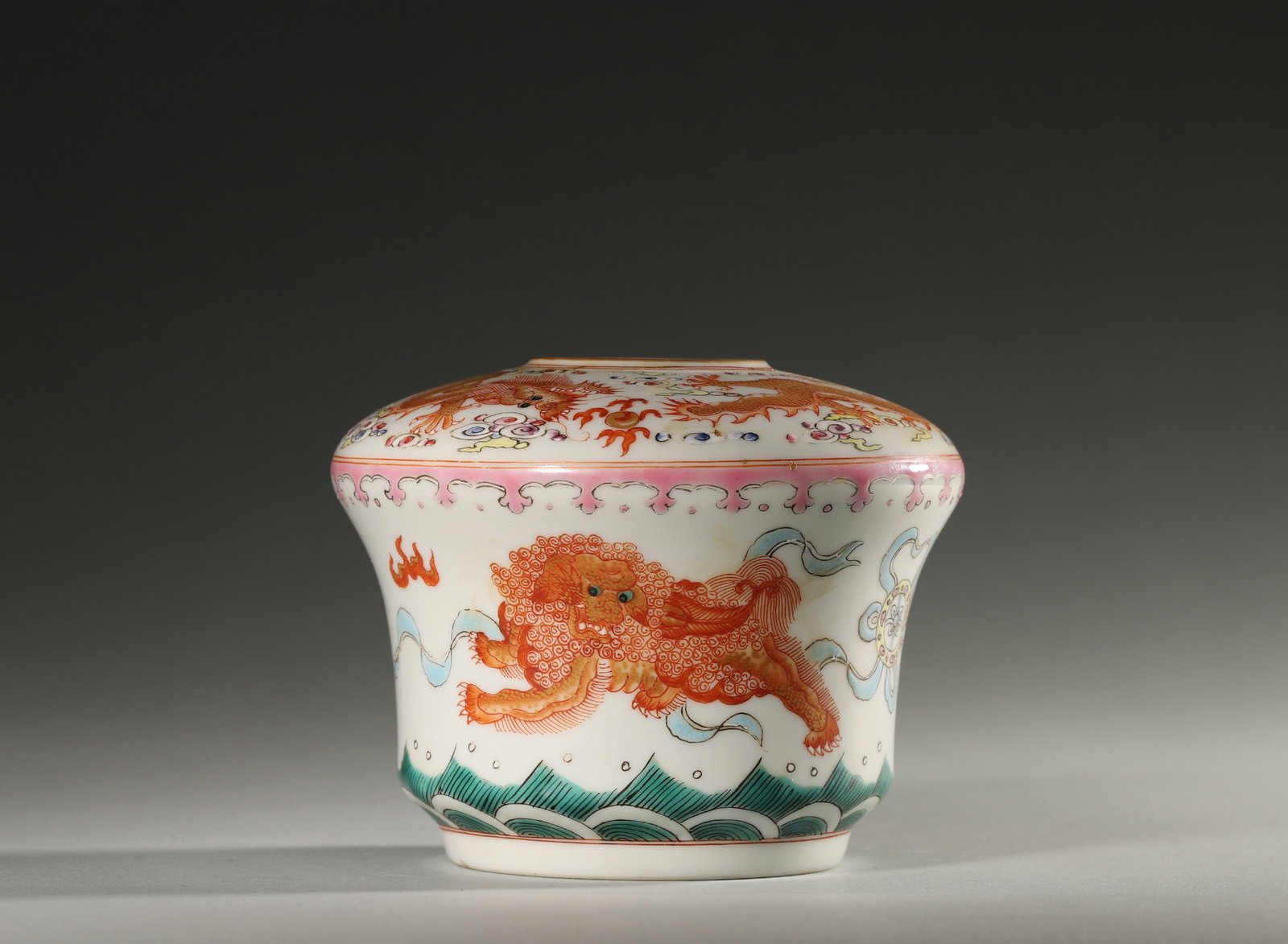 A FAMILLE-ROSE 'LION AND DRAGON' WATER POT: A waisted porcelain water pot painted in famille rose and iron red with a lion and dragon. The base bears a six-character mark reading 'Da Qing Yongzheng Nian Zhi'. Diam. 11 cm; Ht. 8 cm.