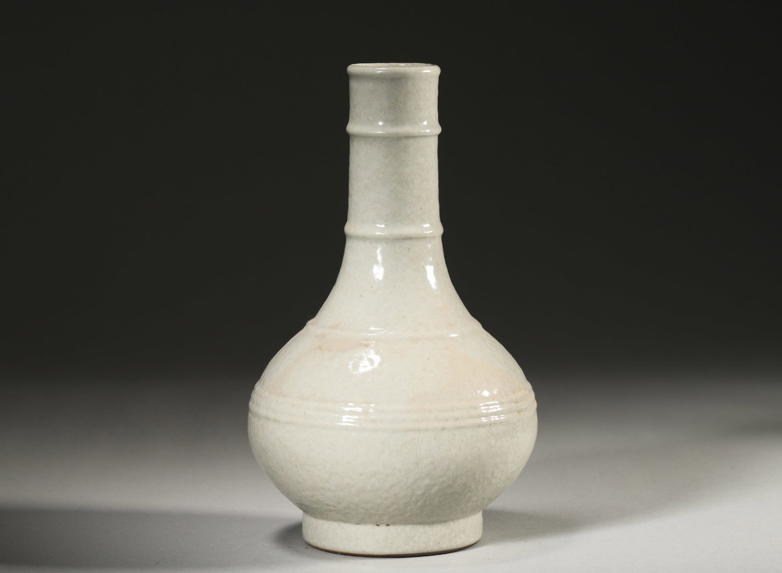 A GE-TYPE CRACKLE-GLAZED 'BAMBOO' VASE WITH BOWSTRING BANDS: A porcelain vase with a bamboo-form long neck and bowstring bands, covered in a white Ge-type crackle glaze. The base bears a mark described in the source as Qianlong. Diam. 10 cm; Ht. 17 cm.