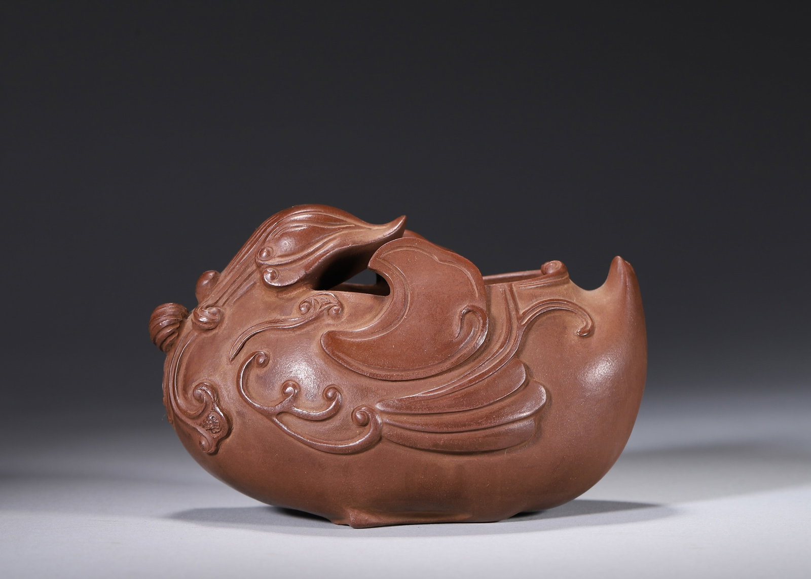 A ZISHA PHOENIX-FORM WATER POT: A zisha water pot modeled in the form of a phoenix with carved wing and scroll motifs. The base bears a poem inscription and a mark in the name of Chen Mingyuan. L. 14 cm; W. 9 cm; Ht. 7 cm.