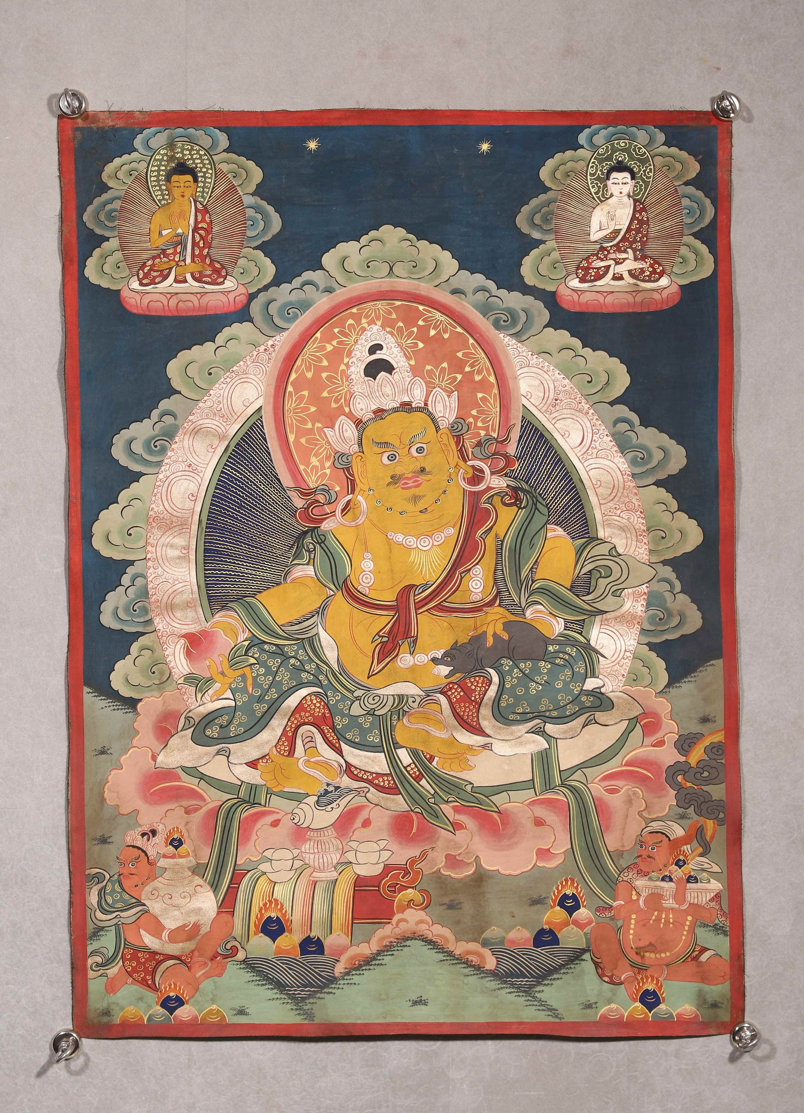 A THANGKA OF YELLOW JAMBHALA: A mineral-pigment thangka depicting Yellow Jambhala seated in lalitasana, holding a mongoose and a wish-granting gem, with Buddhist figures above and attendants below. The reverse bears red Tibetan