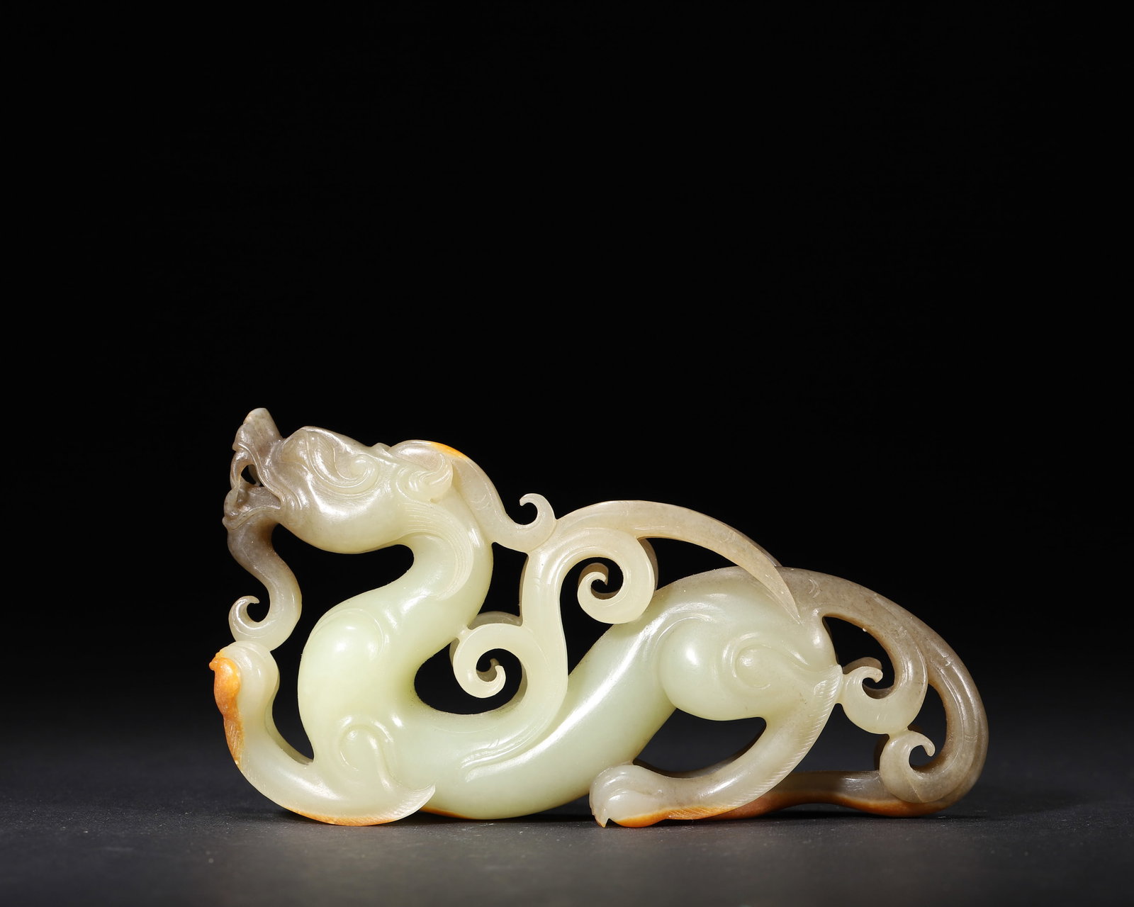 A WHITE JADE OPENWORK 'DRAGON' ORNAMENT: A white jade ornament carved in openwork with a dragon and areas of russet skin. L. 12 cm; Ht. 6.5 cm; Wt. 153 g.