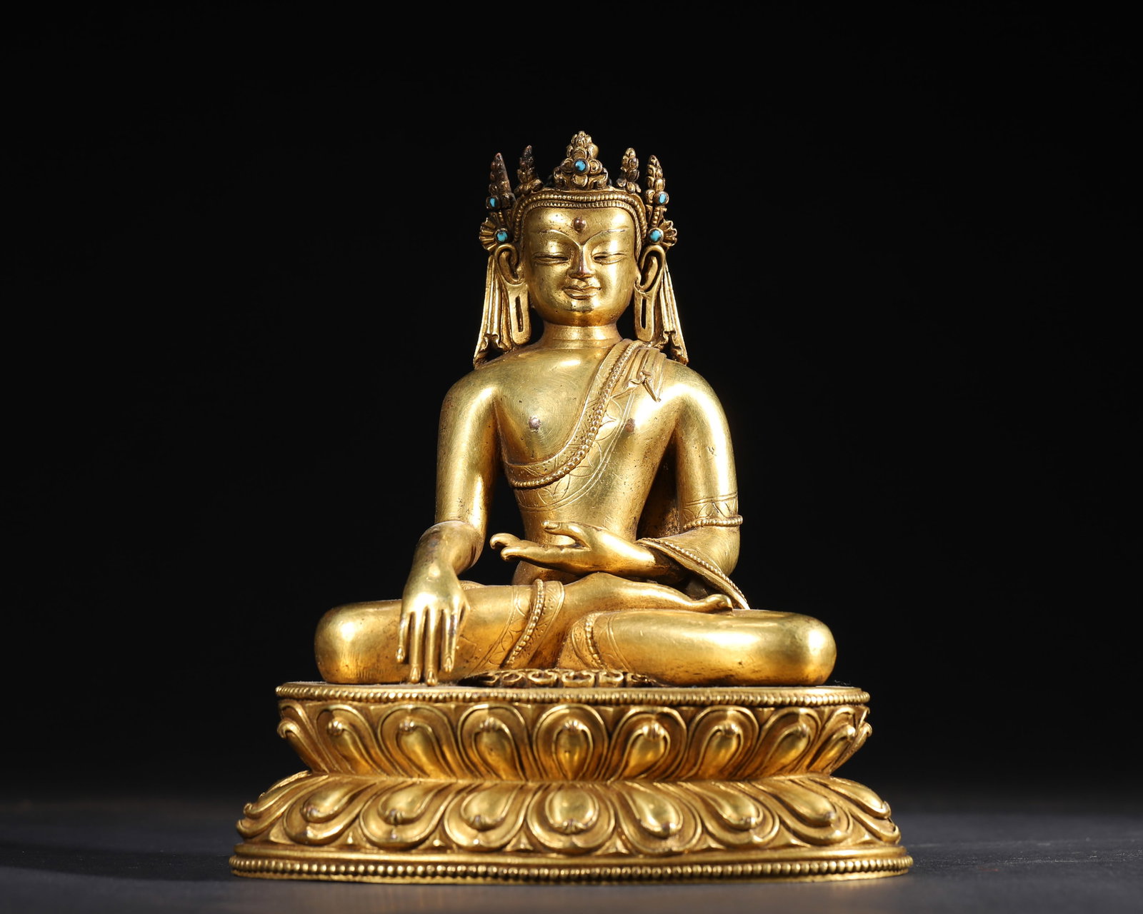 A GILT-BRONZE CROWNED SHAKYAMUNI BUDDHA: A gilt-bronze figure of crowned Shakyamuni Buddha seated on a lotus base, wearing a five-leaf crown, the right hand in bhumisparsha mudra and the left in meditation mudra. The base bears a crossed-vaj