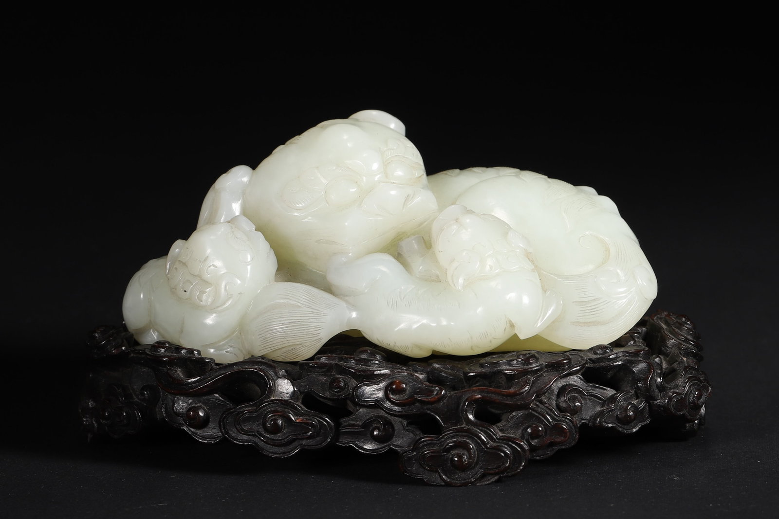 A WHITE JADE 'LION AND CUBS' GROUP: A white jade group carved with a large lion and two cubs, with incised mane details. L. 10.4 cm; W. 7.3 cm; Ht. 4.3 cm; Wt. 383 g. Note: With a hardwood stand.