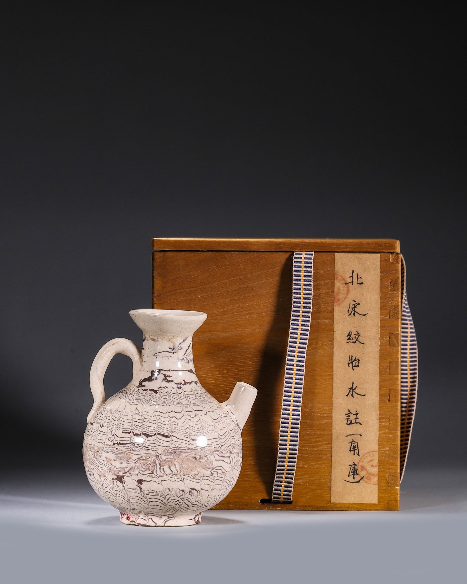 A MARBLED-CLAY EWER: A marbled-clay ewer with a rounded body, flared mouth, curved handle and short spout, with feather-like streaks of brown and white clay. Diam. 9 cm; Ht. 12 cm. Note: With a box and label.