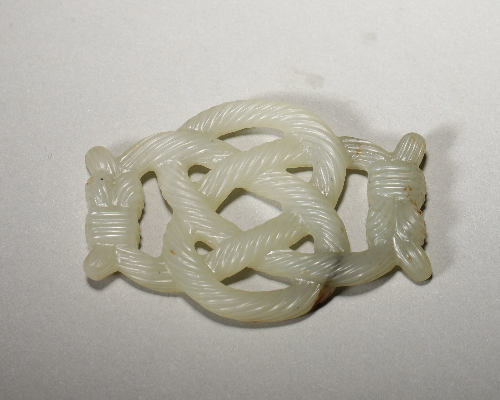 A JADE OPENWORK ETERNAL-KNOT PENDANT: A jade pendant carved in openwork as an eternal knot, with detailed rope-like lines and areas of surface patination. L. 6.7 cm; W. 4.5 cm; Wt. 27 g. Note: By repute, the eternal-knot form is