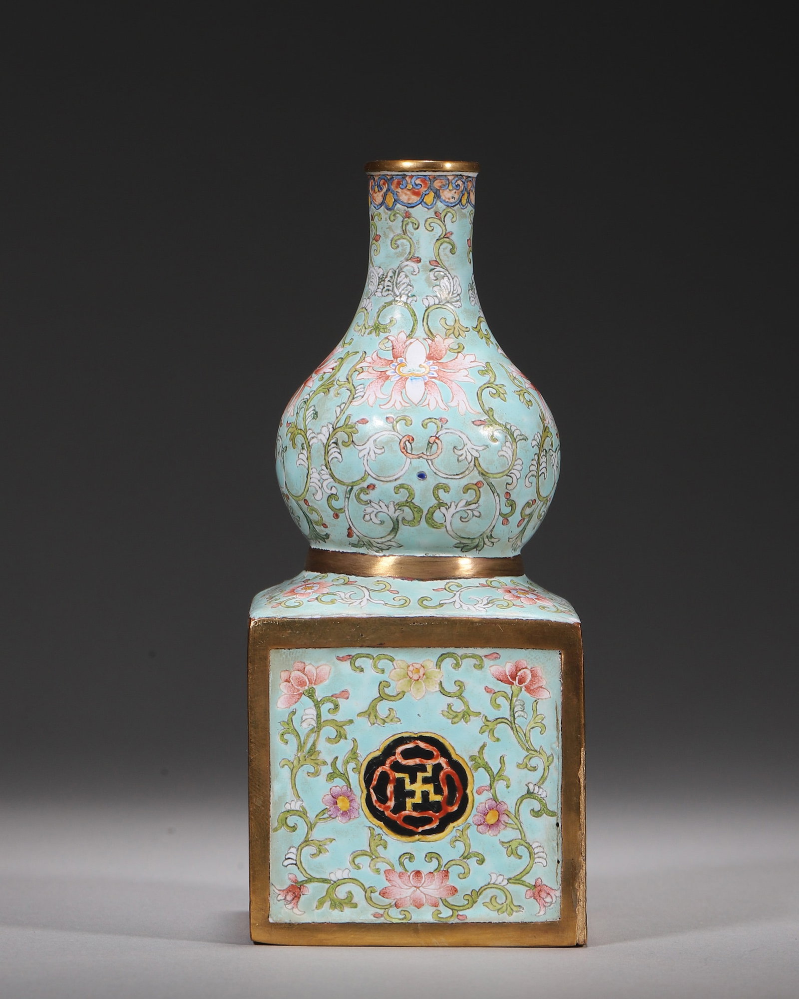 A COPPER-BODY PAINTED-ENAMEL GOURD VASE ON SQUARE BASE: A copper-body painted-enamel gourd-form vase on a square base, with gilt rims, decorated with scrolling lotus on a turquoise ground and a central wan-symbol panel. The base bears a mark described in t