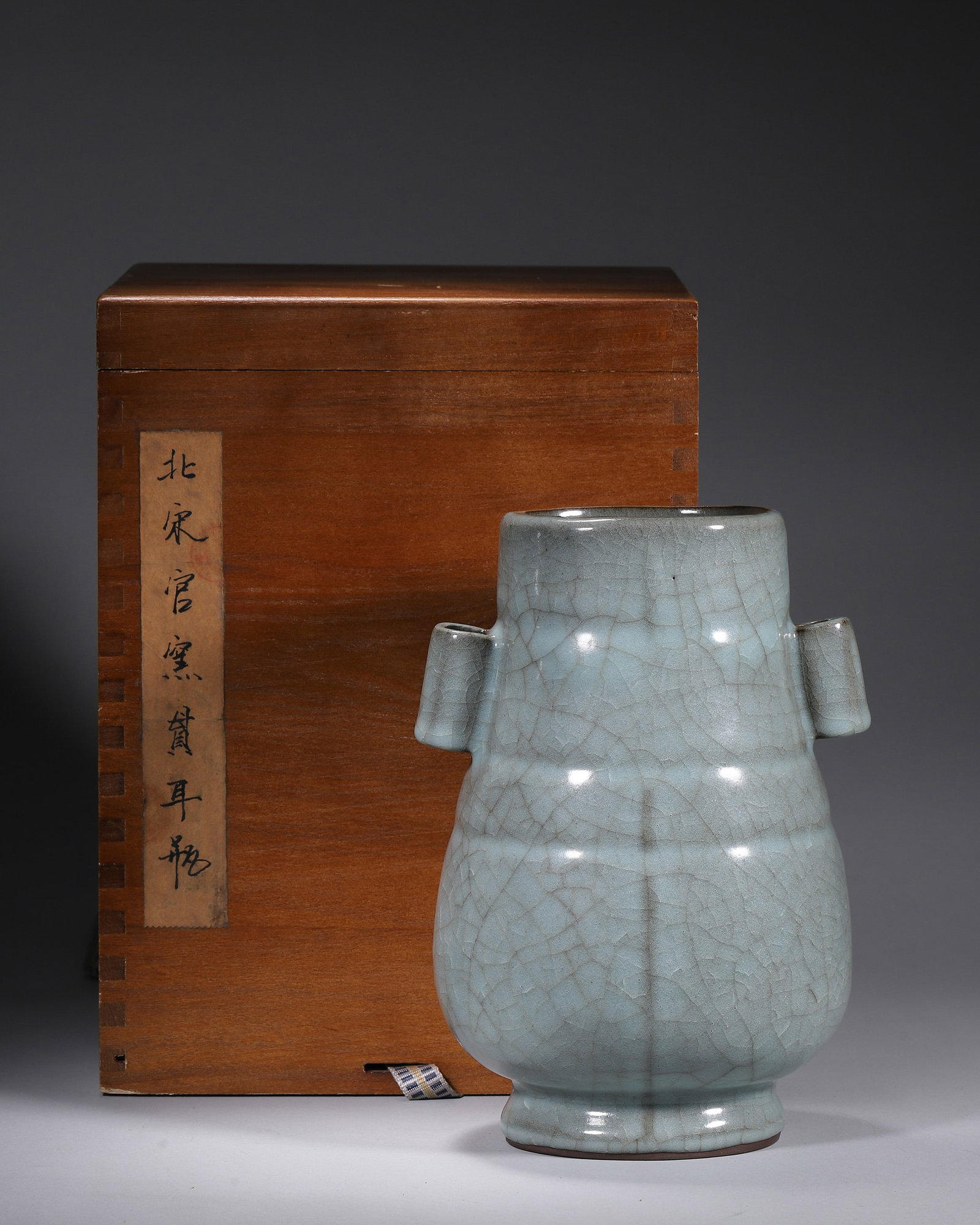 A GUAN-TYPE CELADON VASE WITH TUBULAR HANDLES AND BOWSTRING BANDS: A celadon-glazed porcelain vase with twin tubular handles and raised bowstring bands, covered in a grey-blue Guan-type crackle glaze with a dark foot. The base bears collector marks. L. 13 cm; W. 12 c