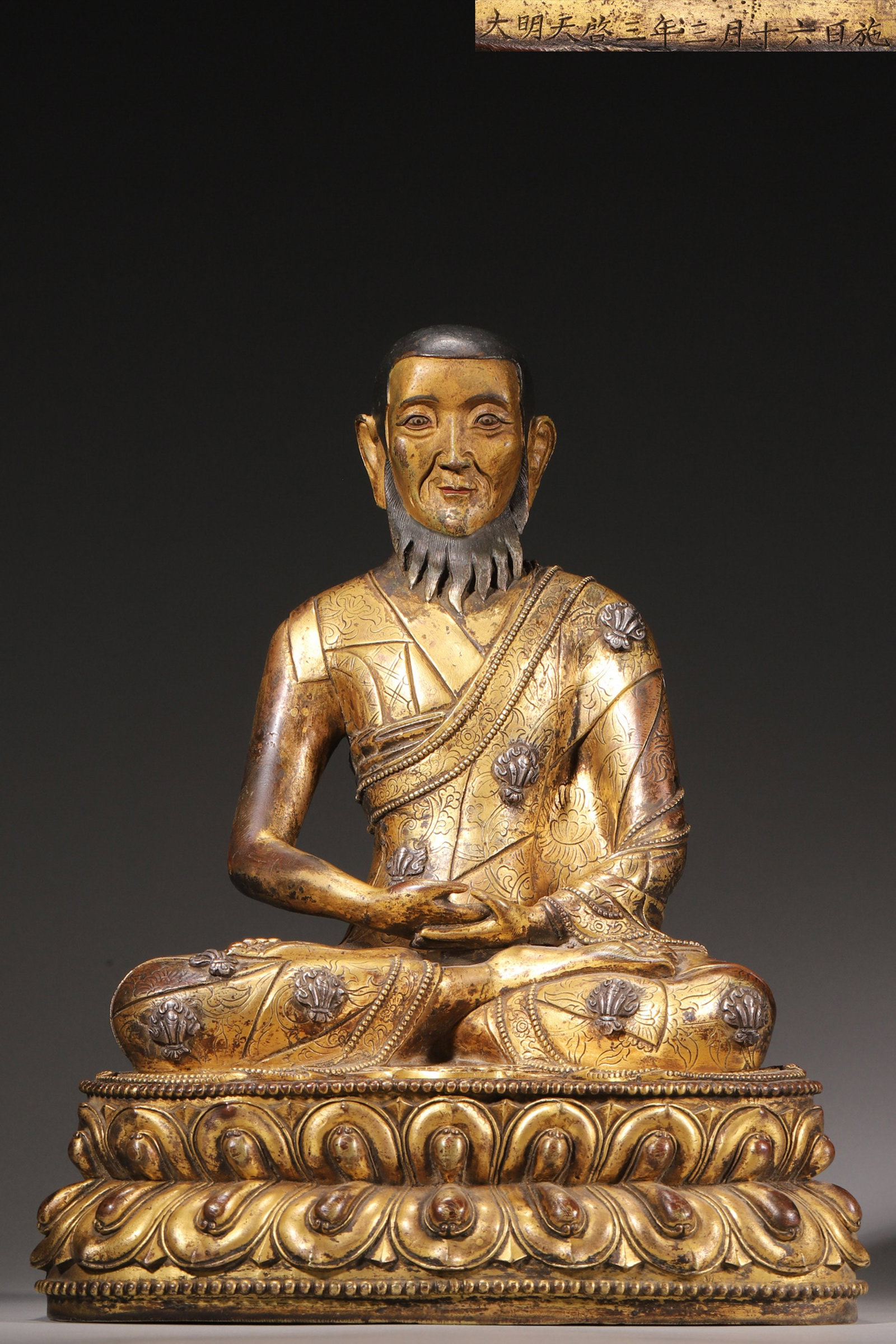 A SILVER-INLAID GILT-BRONZE LAMA FIGURE: A silver-inlaid gilt-bronze lama figure seated in full lotus posture with the hands in meditation mudra, with patterned robes and a lotus base. L. 22 cm; W. 16 cm; Ht. 28 cm; Wt. 5,153 g.