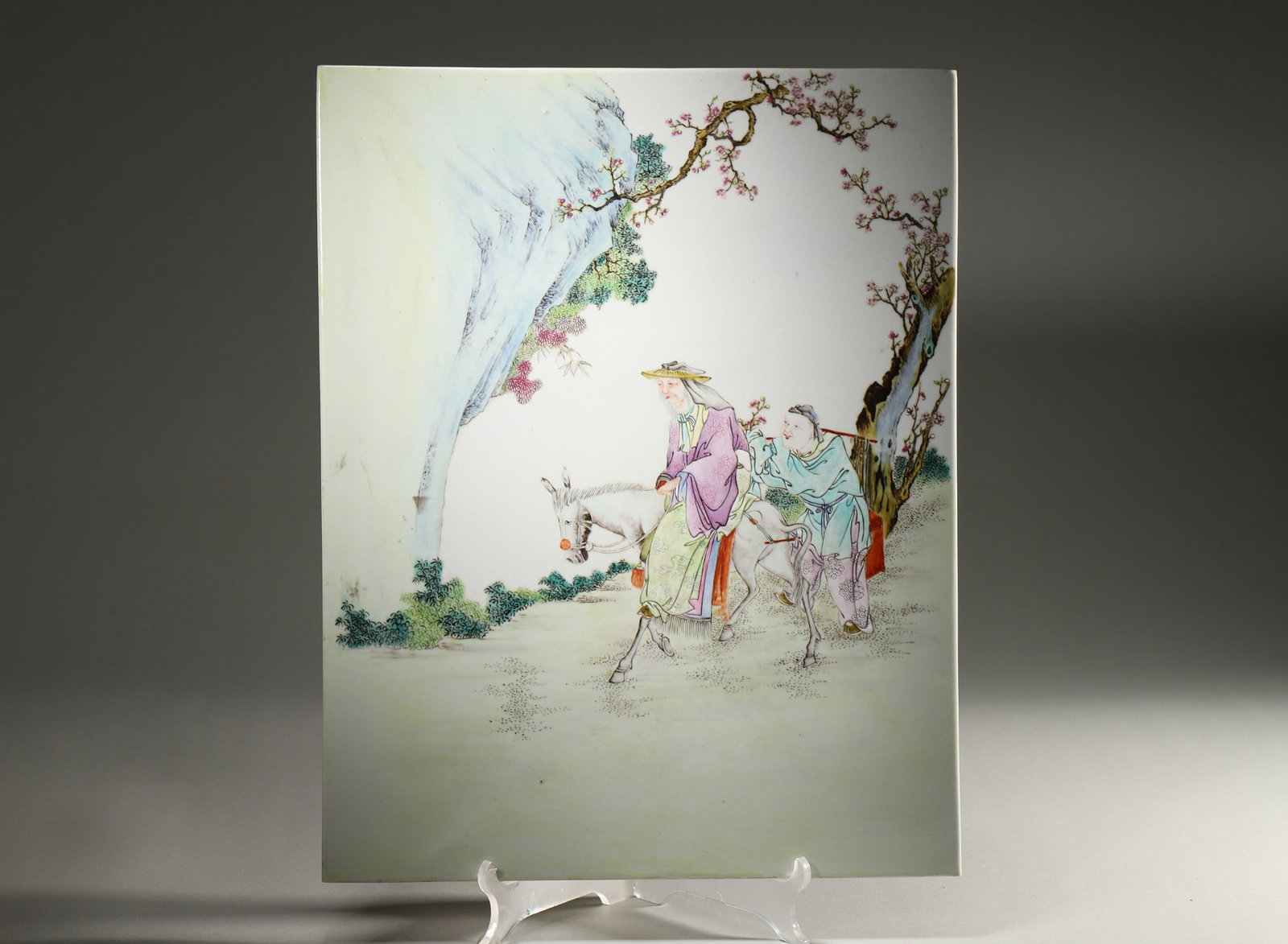 A FAMILLE-ROSE 'SEEKING PLUM BLOSSOMS IN THE SNOW' PORCELAIN PLAQUE: A rectangular famille-rose porcelain plaque depicting an elderly man riding a donkey with an attendant in a wintry landscape. L. 39 cm; W. 30 cm.