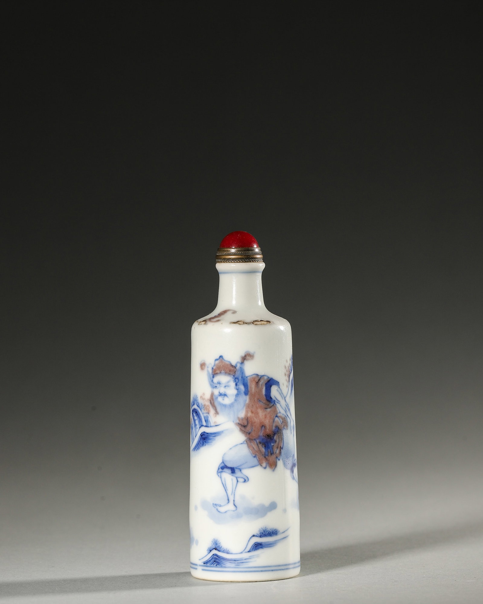 A BLUE-AND-WHITE AND UNDERGLAZE-RED FIGURAL PORCELAIN SNUFF BOTTLE: A blue-and-white and underglaze-red porcelain snuff bottle decorated with a figural scene. Diam. 3 cm; Ht. 10.7 cm.