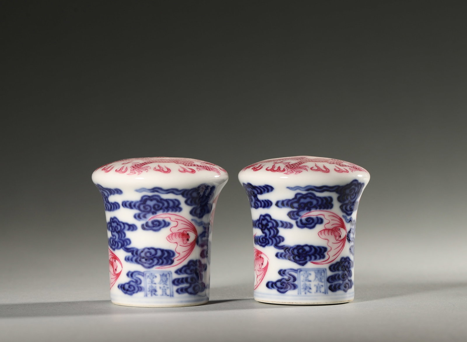 A PAIR OF BLUE-AND-WHITE AND IRON-RED 'BAT' PORCELAIN SCROLL ENDS: A pair of porcelain scroll ends decorated in underglaze blue and iron red with bat motifs. Diam. 5.3 cm; Ht. 5.4 cm.