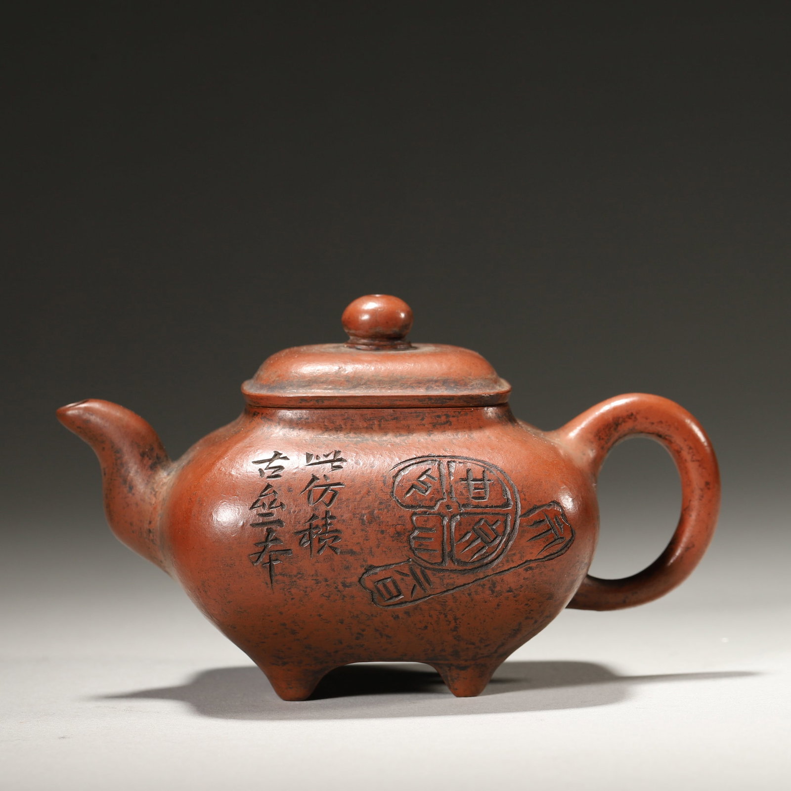 A ZISHA CHUANLU-FORM TEAPOT WITH BIRD, PLUM AND INSCRIPTION: A purple-clay zisha teapot of square chuanlu form, with a bead-form finial, short spout, loop handle and four feet, carved with a bird on plum and an inscription. The base bears a mark in the name of