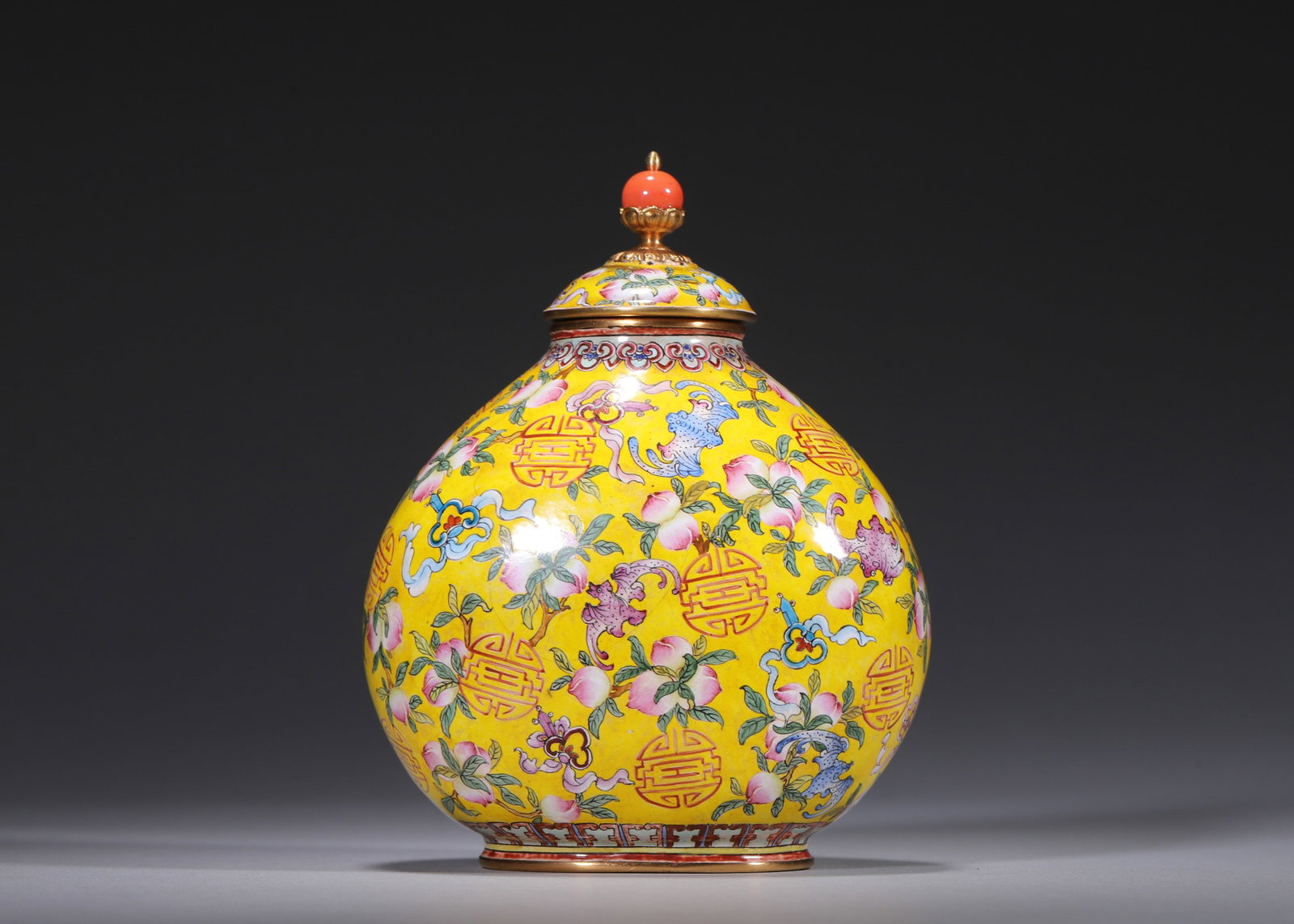 A GILT-BRONZE PAINTED-ENAMEL YELLOW-GROUND 'PEACH, BAT AND SHOU' JAR AND COVER: A gilt-bronze painted-enamel jar and cover with gilt borders and a red finial, decorated with peaches, bats and shou emblems on a yellow ground. The base bears a mark described in the source as