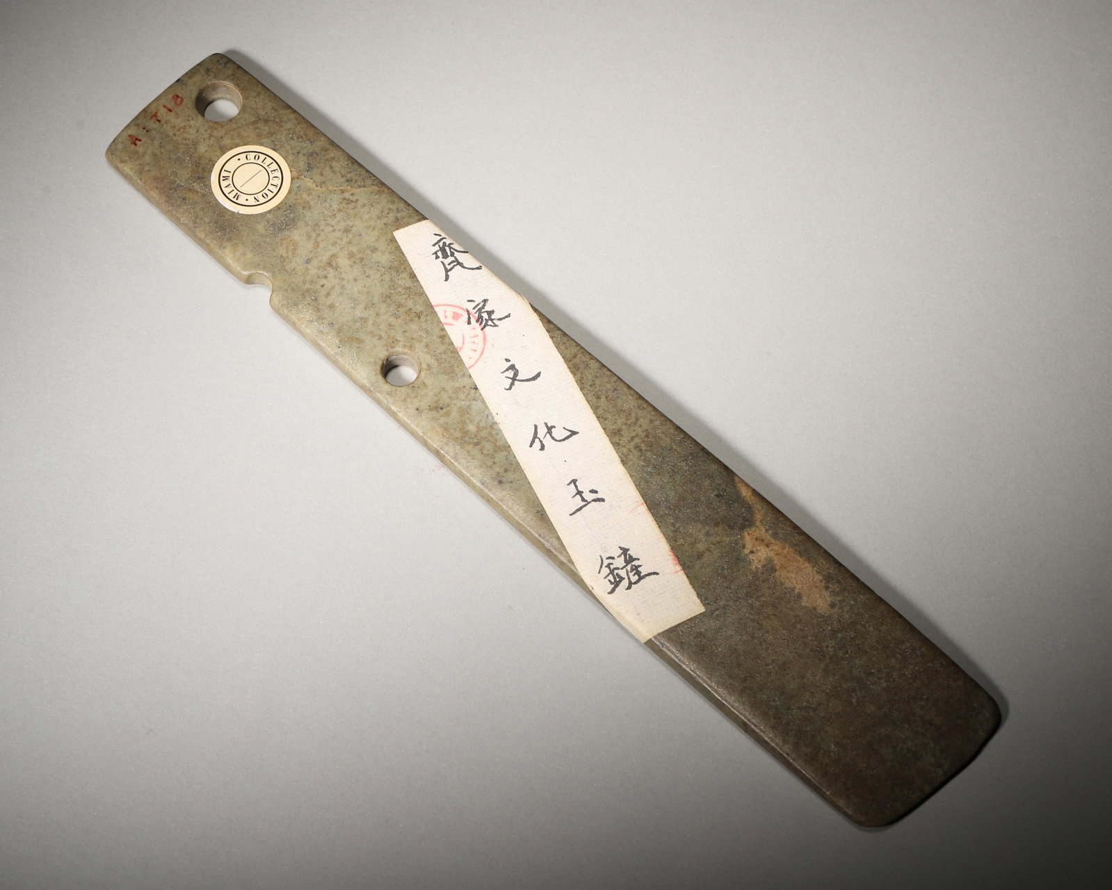 A JADE ZHANG, QIJIA CULTURE: A jade zhang of elongated form with a raised ridge and perforation, with a plain surface. L. 26.2 cm; W. 4.7 cm; Wt. 254 g. Note: With a label. By repute, associated with ritual and ceremonial use.