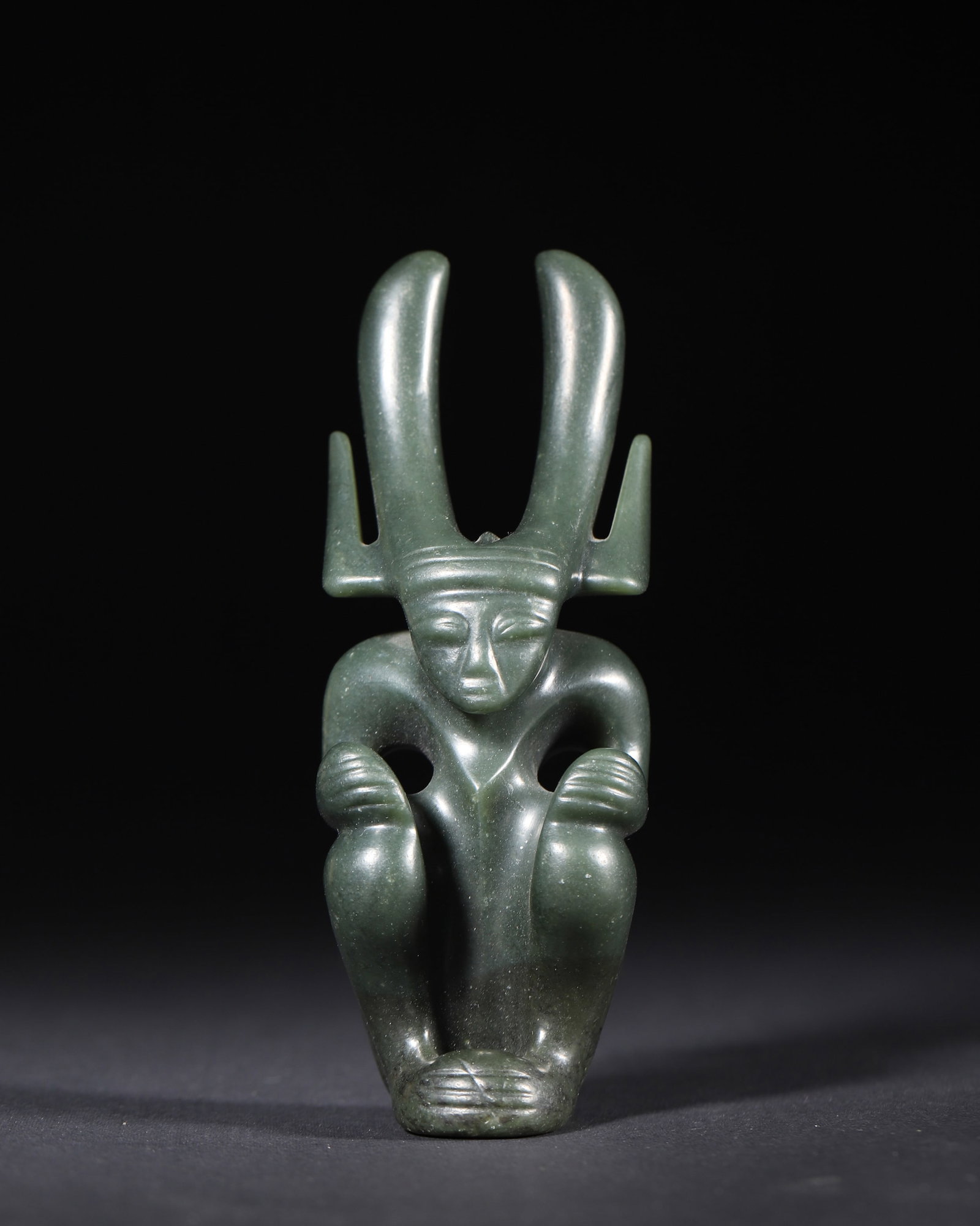 A GREEN JADE ANTHROPOMORPHIC FIGURE, HONGSHAN CULTURE: A green jade figure carved in seated anthropomorphic form with a tall horned headdress. L. 5 cm; W. 5 cm; Ht. 13 cm; Wt. 266 g. Note: By repute, associated with Hongshan culture.