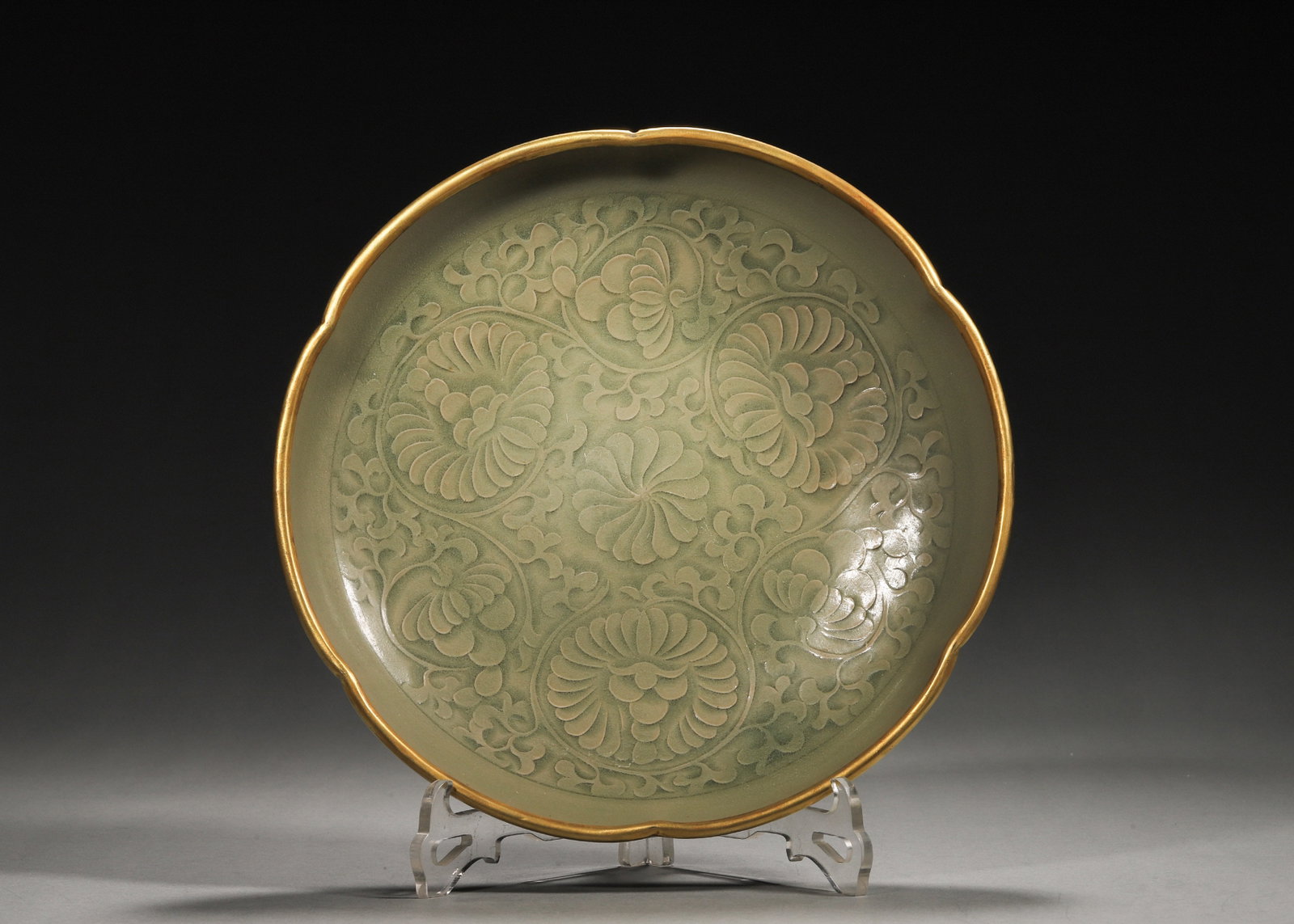A YAOZHOU-TYPE CELADON-GLAZED CARVED 'CHRYSANTHEMUM' FOLIATE-RIM DISH: A foliate-rim porcelain dish covered in a celadon glaze, the interior carved with intertwined chrysanthemum motifs and the rim with gilt-metal mounting. The exterior is plain and the base unglazed.