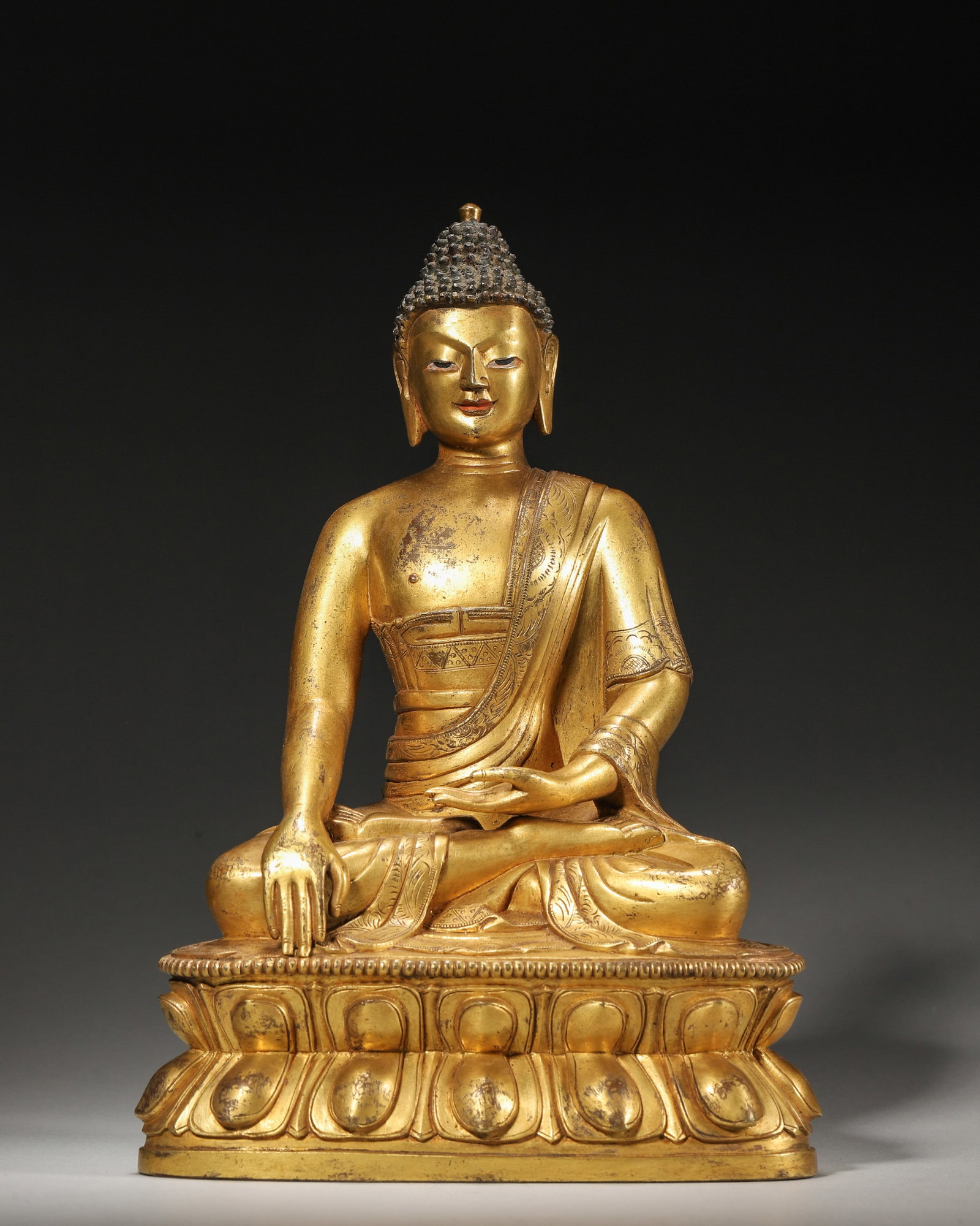 A GILT-BRONZE FIGURE OF SHAKYAMUNI BUDDHA: A gilt-bronze figure of Shakyamuni Buddha seated on a lotus base. W. 14 cm; Ht. 21 cm; Wt. 2,148 g.