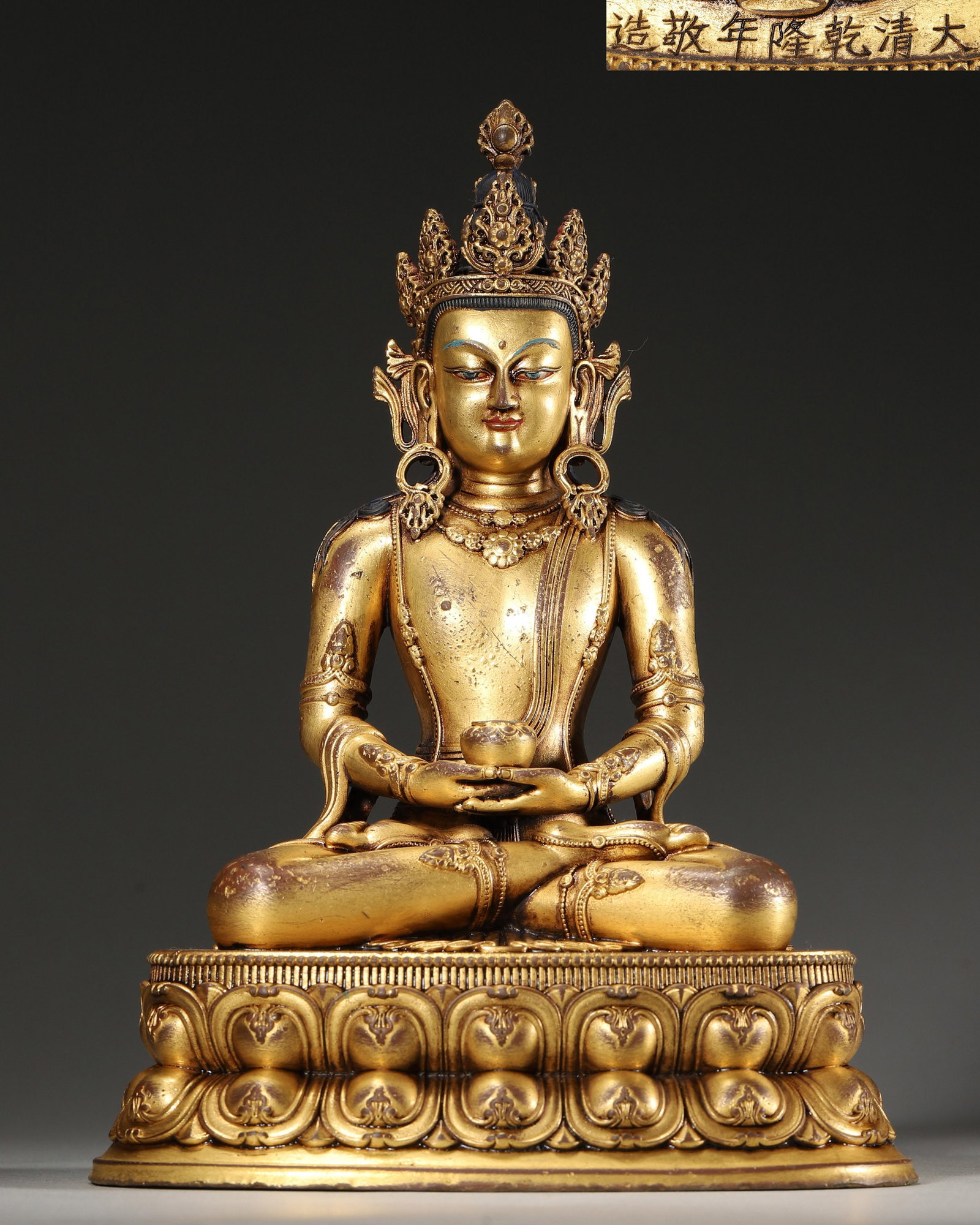 A GILT-BRONZE FIGURE OF AMITAYUS: A gilt-bronze figure of Amitayus seated cross-legged on a lotus base, holding a vase. The base bears an inscription reading 'Da Qing Qianlong Nian Jing Zao'. L. 15 cm; W. 11 cm; Ht. 21 cm; Wt. 1,380 g