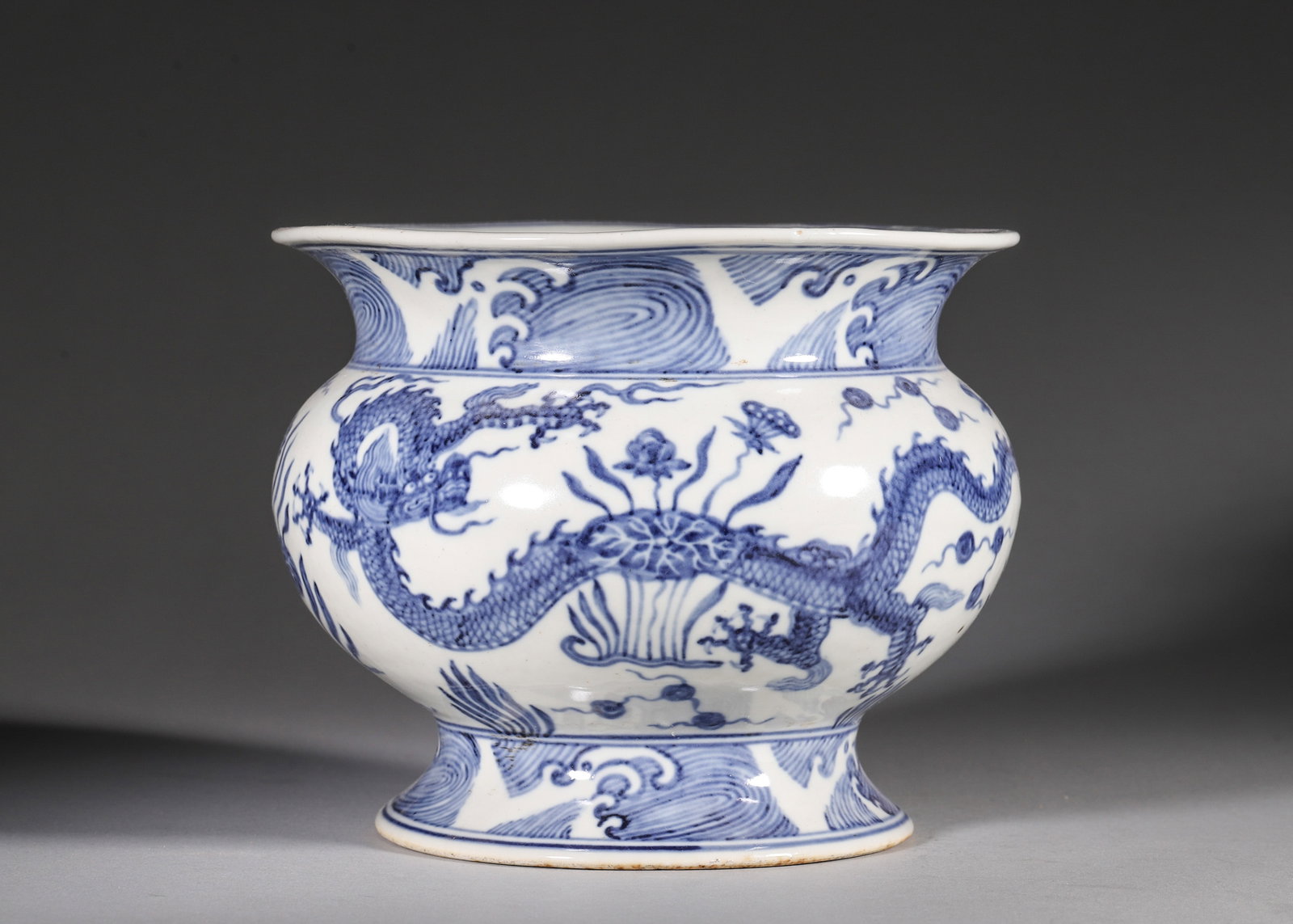 A BLUE-AND-WHITE 'DRAGON AND LOTUS' PORCELAIN JAR: A blue-and-white porcelain jar painted with two dragons amid lotus and aquatic plants, with wave borders to the mouth and foot. The base bears a six-character mark described in the source as Xuande.