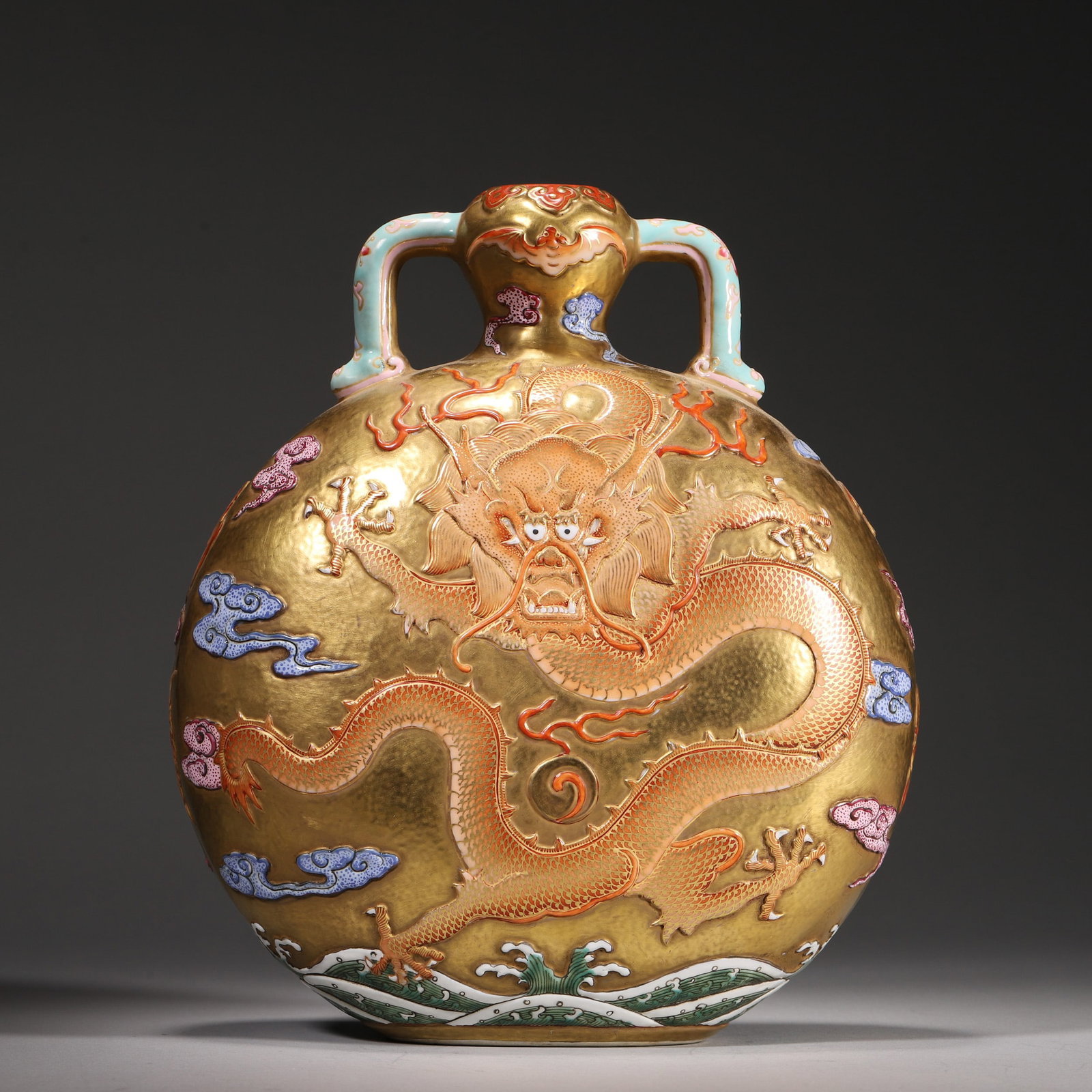 A GILT-GROUND RELIEF 'DRAGON AND CLOUD' MOONFLASK WITH RUYI HANDLES: A porcelain moonflask with turquoise-glazed ruyi-form handles, the gilt ground decorated in relief with a dragon amid polychrome clouds and bats, with wave motifs around the lower body. The