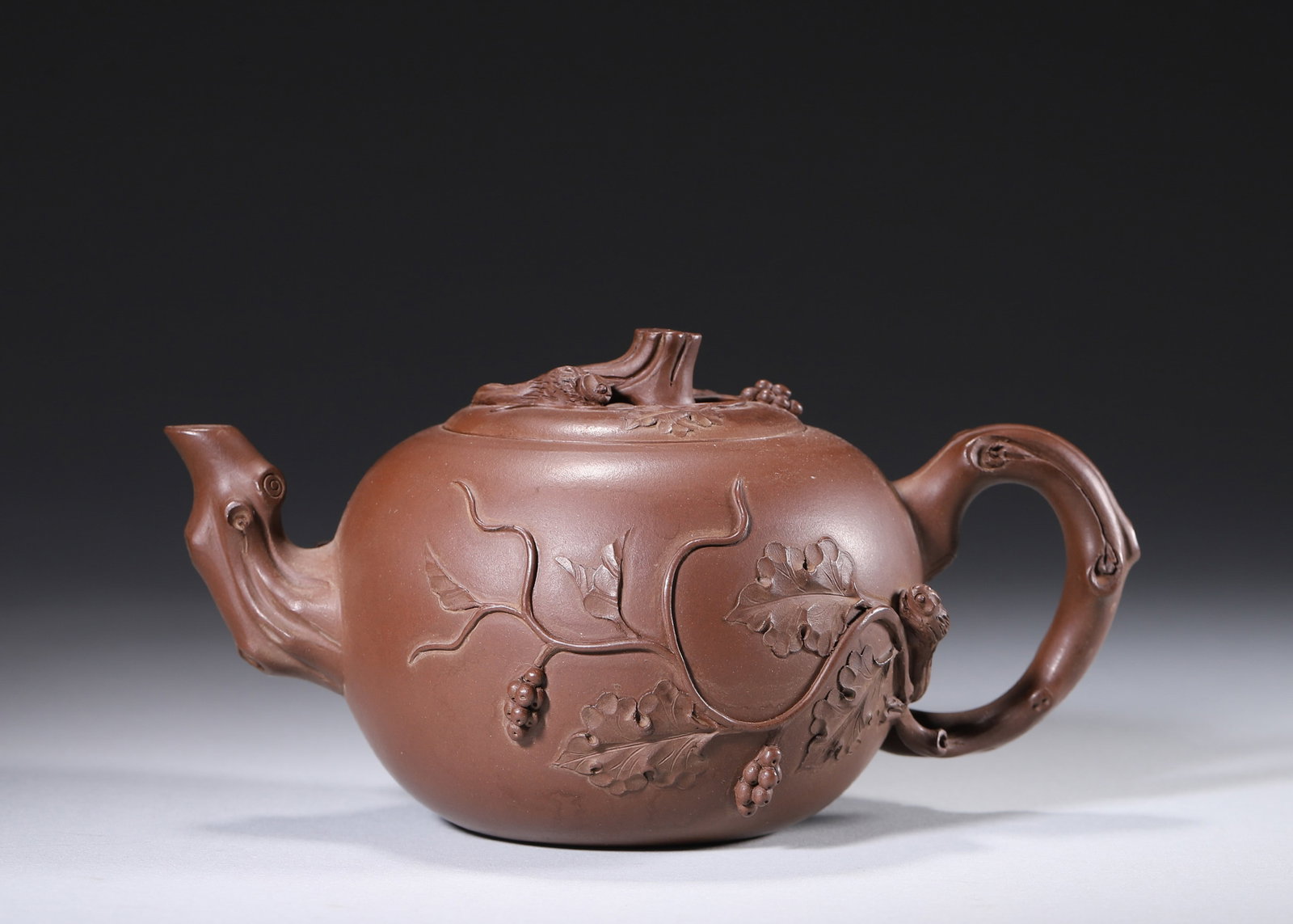 A ZISHA 'SQUIRREL AND GRAPE' TEAPOT: A zisha teapot modeled with tree-textured spout, handle and finial, decorated in relief with grape vines, leaves and squirrels. The base and inner cover bear seals in the name of Zhu Kexin. L. 17 cm;