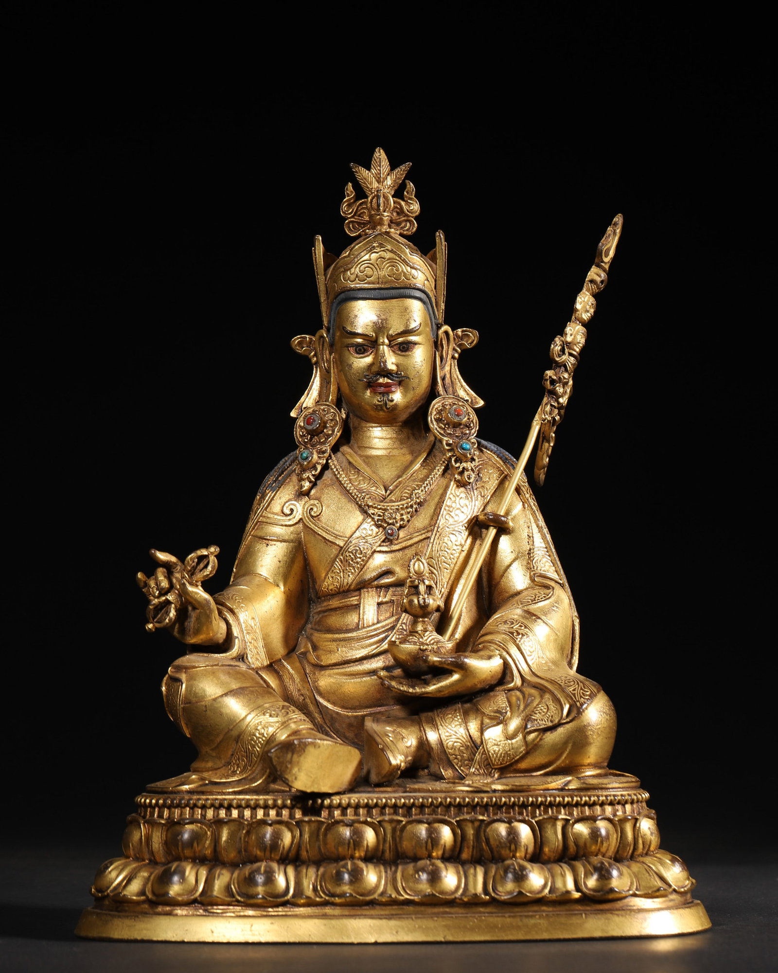 A GILT-BRONZE FIGURE OF PADMASAMBHAVA: A gilt-bronze figure of Padmasambhava seated on a lotus base, with rich gilding and a crossed-vajra motif to the base. Dimensions: 18 x 13 x 22 cm; Wt. 2,020 g.