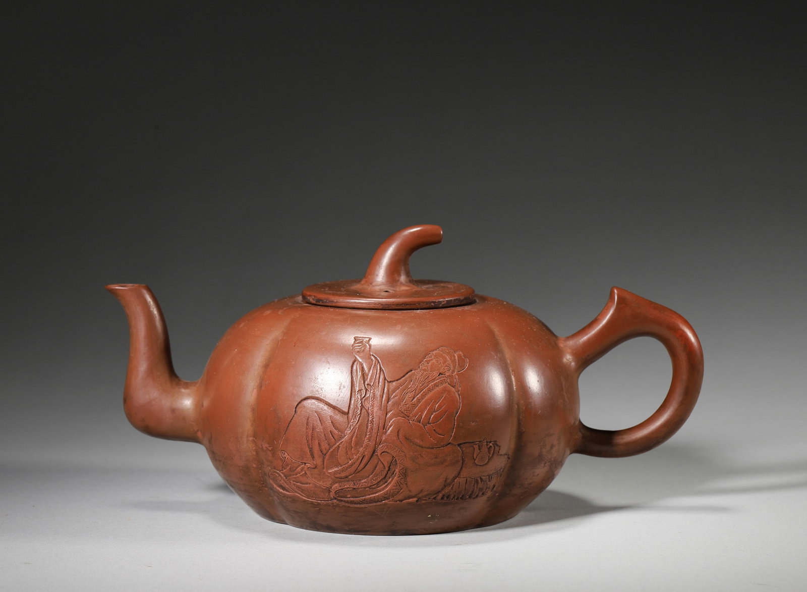 A ZISHA PUMPKIN-FORM TEAPOT WITH FIGURE AND POEM: A zisha teapot of pumpkin form with a stem-form finial, one side molded with a drinking figure and the other carved with a poem. The base bears a square seal. L. 18.5 cm; W. 12 cm; Ht. 10 cm; Wt. 413
