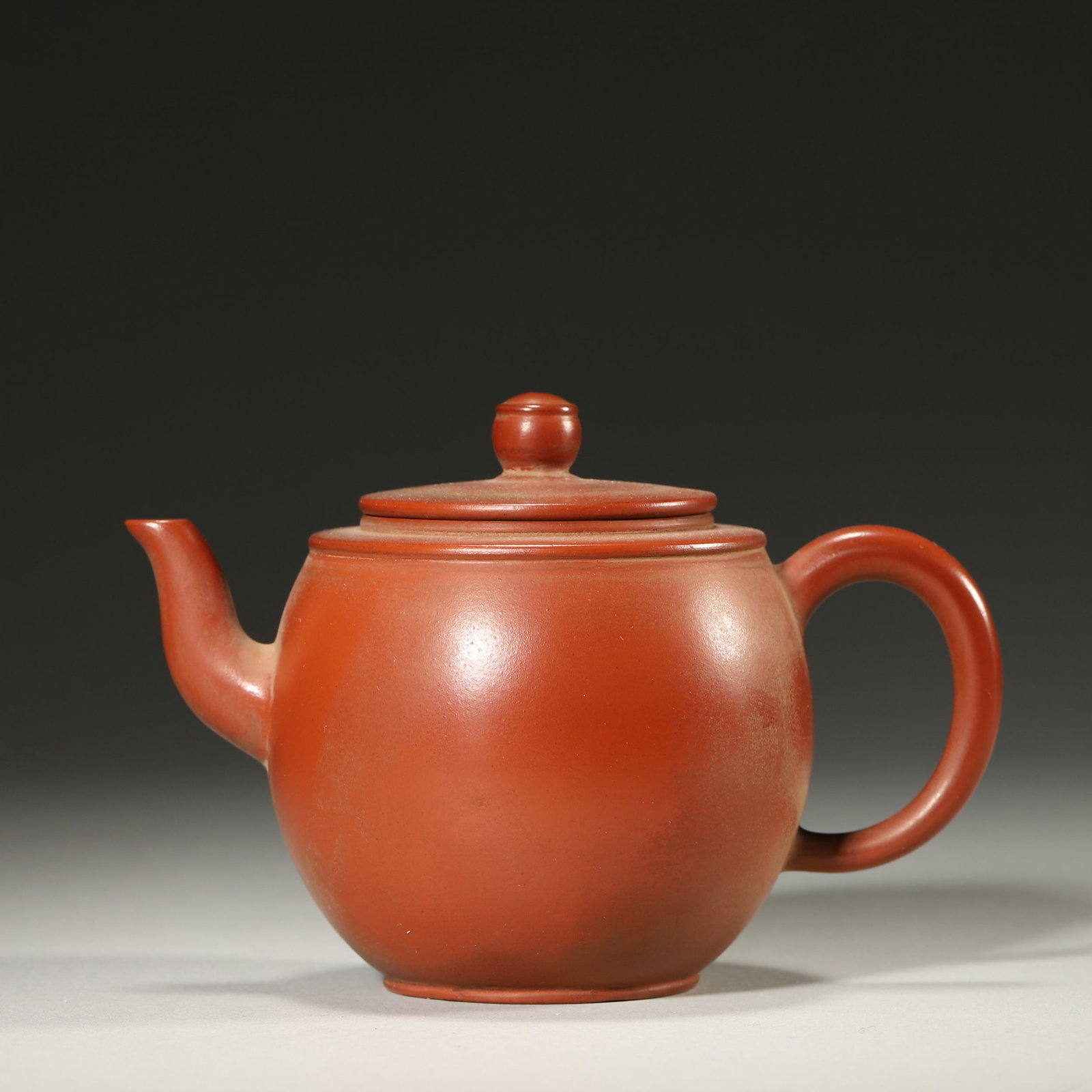A ZHUNI ZISHA ROUND TEAPOT: A zhuni zisha teapot of rounded form with a short spout, loop handle and bead-form finial. The base bears a mark in the name of Mengchen. L. 12 cm; W. 8 cm; Ht. 8 cm.