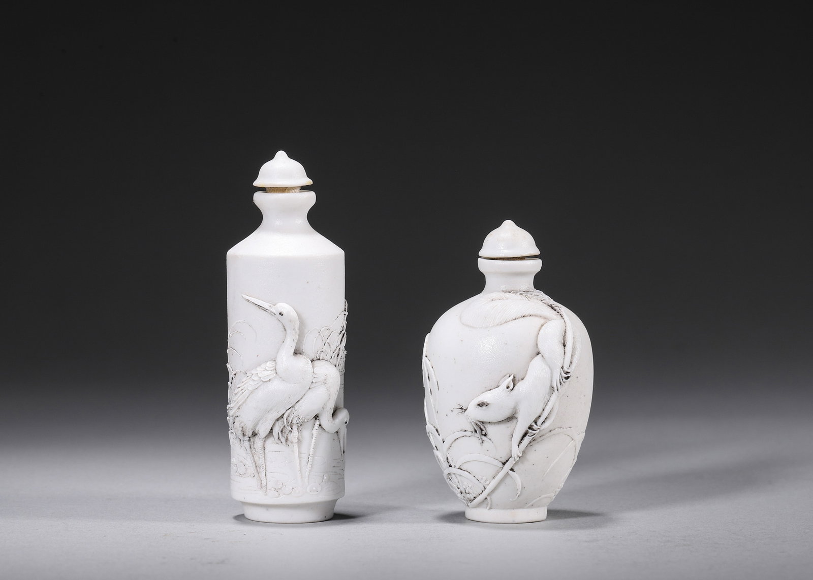 A PAIR OF WHITE-GLAZED RELIEF 'CRANE AND RAT' PORCELAIN SNUFF BOTTLES: A pair of white-glazed porcelain snuff bottles carved in relief, one with cranes among pines and the other with a rat and grass motifs, with porcelain covers. The bases bear seals in the name of Chen