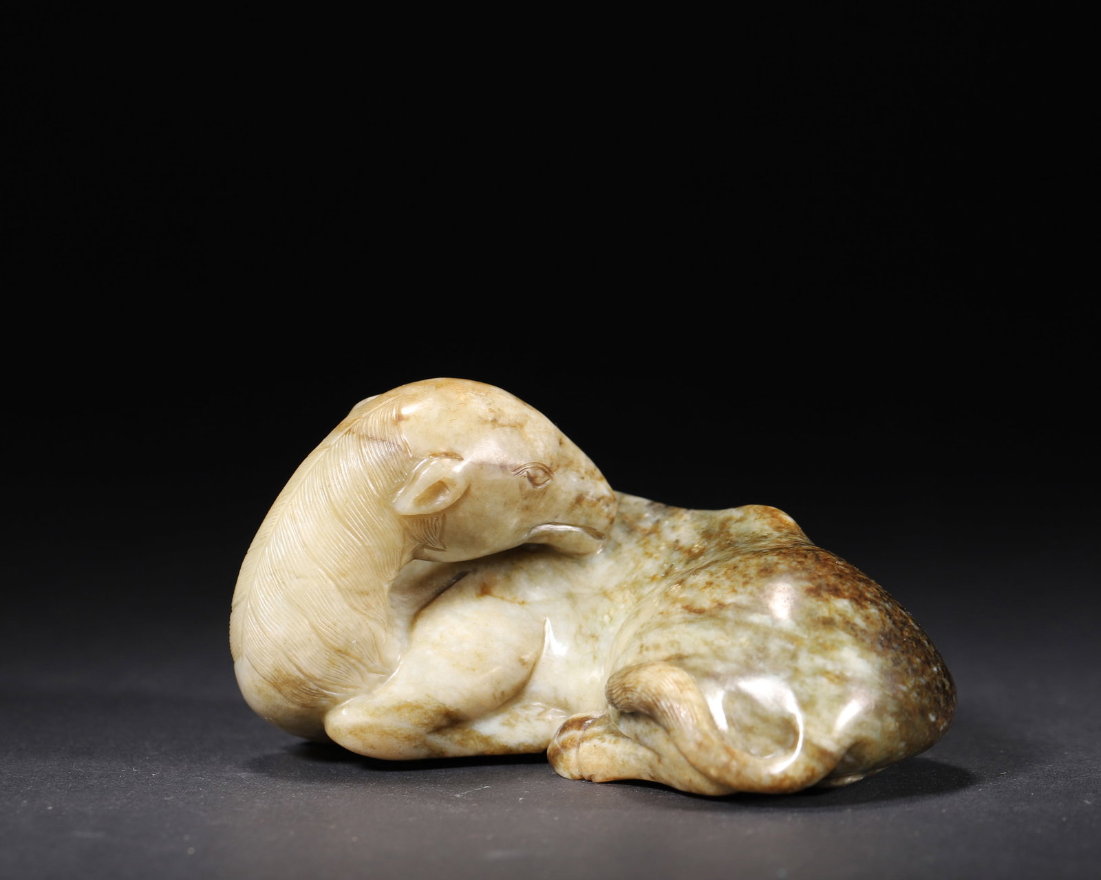 A JADE 'RECUMBENT HORSE' ORNAMENT: A jade ornament carved as a recumbent horse with its head turned, with areas of reddish-brown coloration. L. 10.5 cm; W. 7.5 cm; Ht. 6 cm; Wt. 441 g.