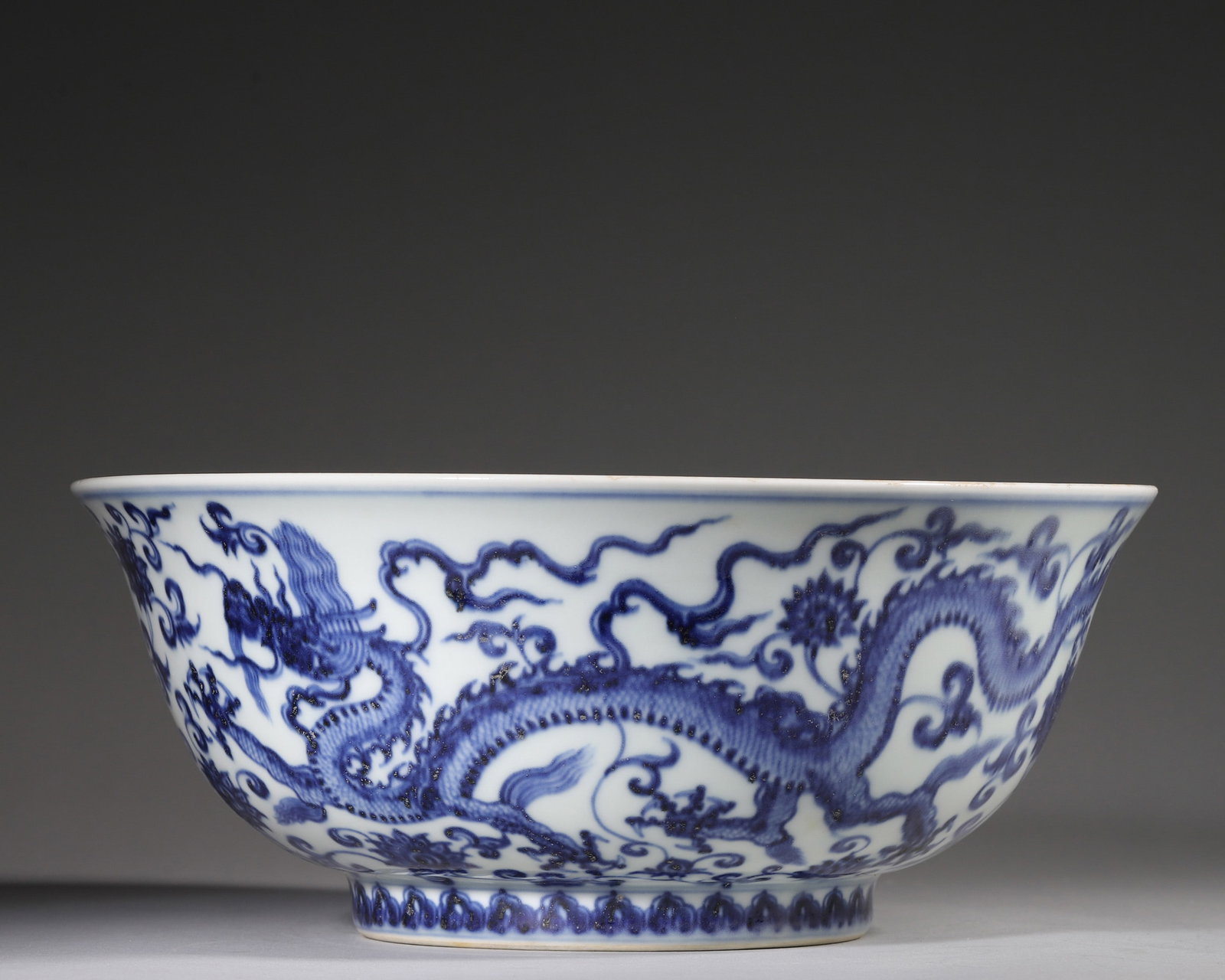 A BLUE-AND-WHITE 'DRAGON AND LOTUS' BOWL: A blue-and-white porcelain bowl painted to the exterior with five dragons amid lotus scrolls and to the interior with a single dragon, with lotus-lappet decoration near the foot. The base bears a
