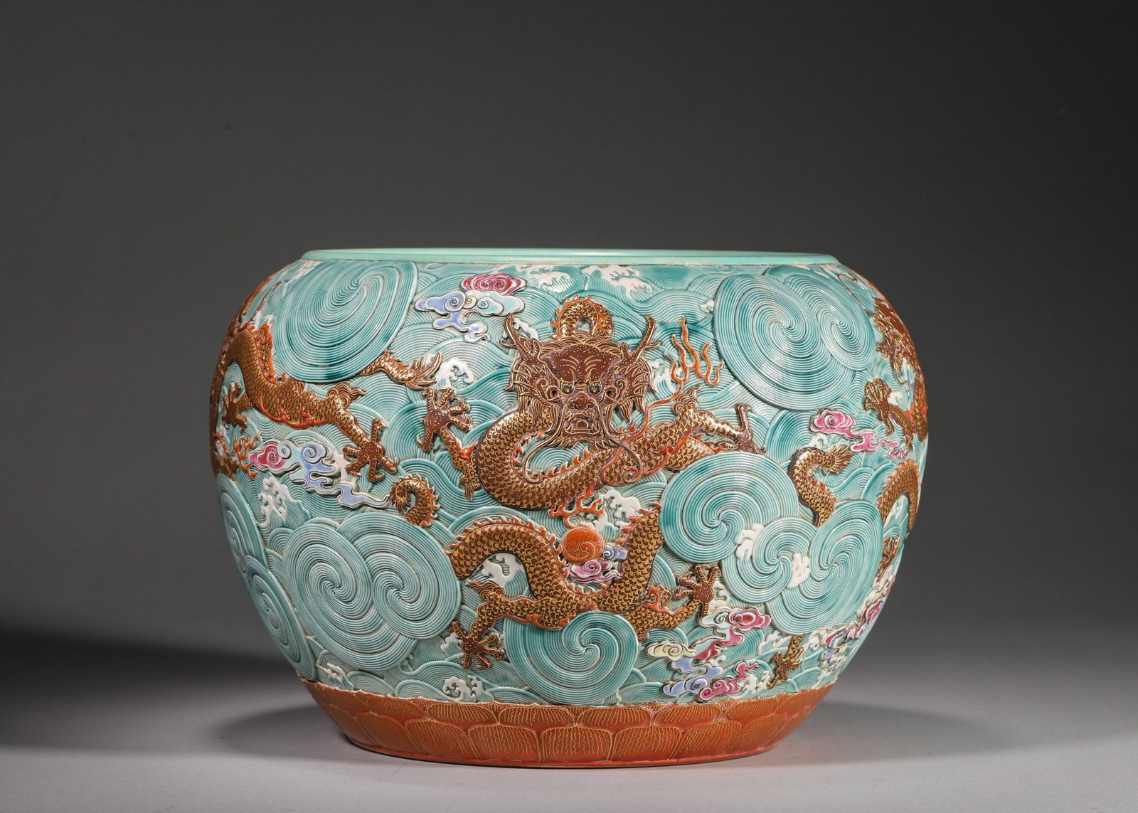 A TURQUOISE-GROUND CARVED 'FIVE DRAGONS' PORCELAIN JAR: A porcelain jar with a turquoise-glazed interior and exterior carved with waves, decorated with five gilt iron-red dragons amid colorful clouds and a lotus border near the base. The base bears a gilt