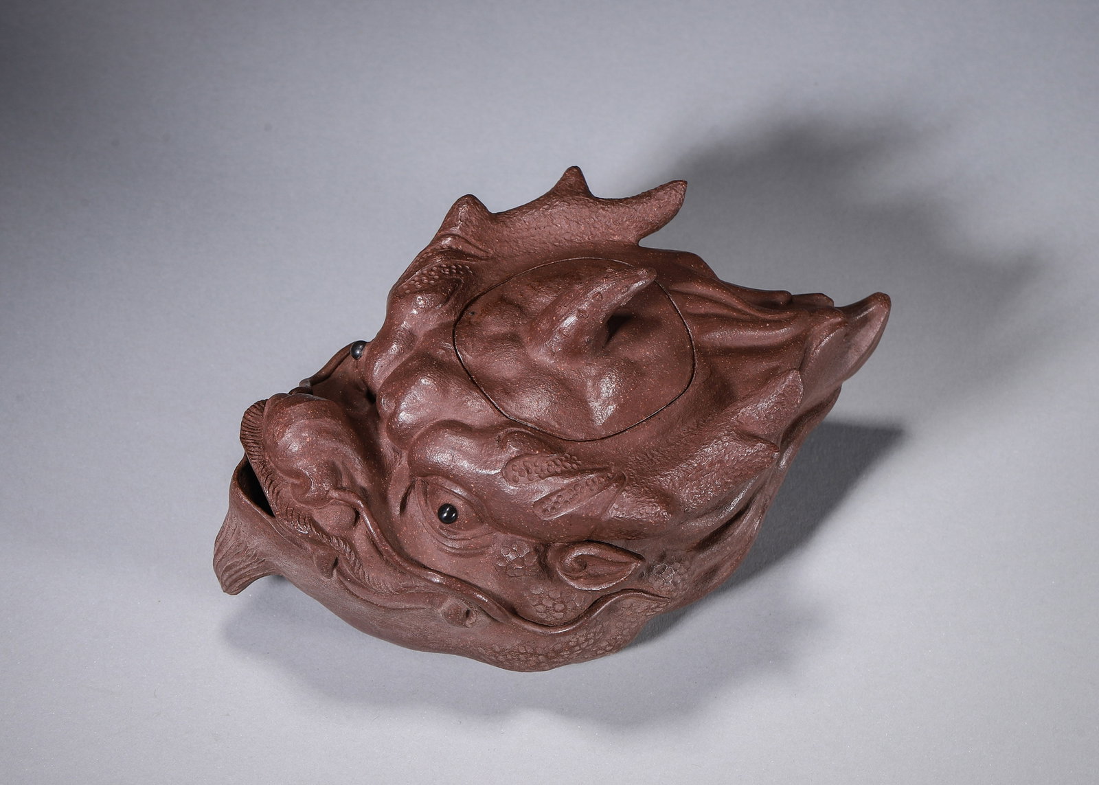 A ZISHA DRAGON-HEAD TEAPOT: A zisha teapot modeled as a dragon head with carved facial features, scales and whiskers. The base bears a mark in the name of Chen Mingyuan. L. 16 cm; W. 10 cm; Ht. 7 cm.