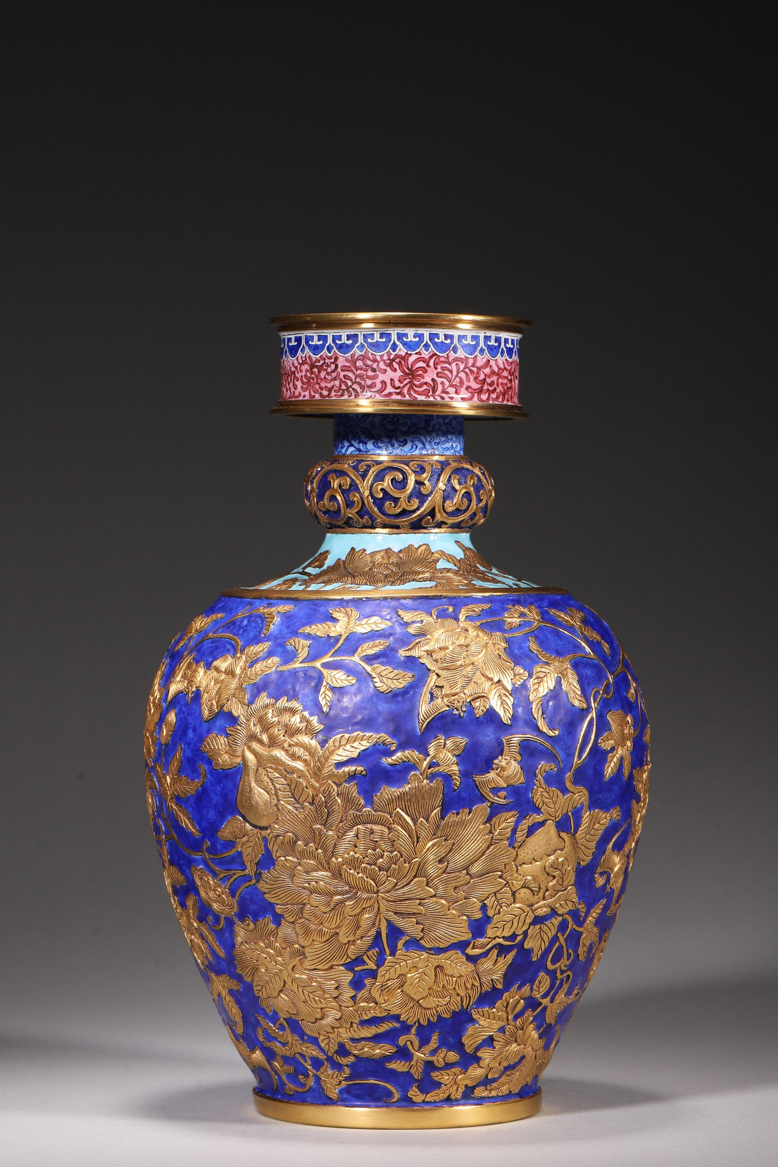 A BLUE-GROUND ENAMELED COPPER VASE WITH CHASED GILT AUSPICIOUS MOTIFS: A copper vase with gilt rim and foot, covered in blue enamel and decorated with chased gilt peonies, peaches and bats, with polychrome enamel bands to the neck. The base bears a mark described in the 