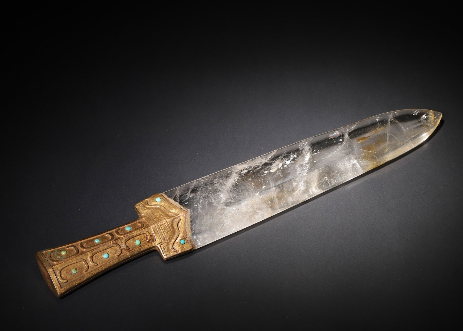 A GILT-BRONZE-MOUNTED ROCK CRYSTAL BLADE ORNAMENT WITH TURQUOISE INLAY: A rock crystal blade-form ornament with a gilt-bronze hilt decorated with archaistic scroll and key-fret motifs and set with turquoise. L. 43 cm; W. 7 cm; Wt. 1,341 g.