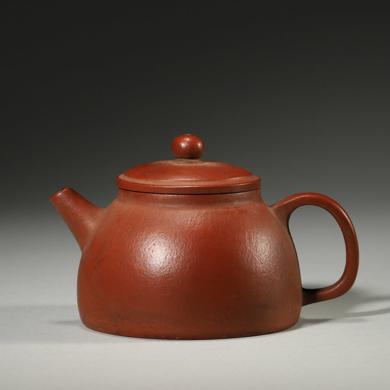 A RED-CLAY ZISHA BELL-FORM TEAPOT: A red-clay zisha teapot with a bell-form body, bead-form finial, short spout and loop handle. The base bears a mark in the name of Mengchen. L. 11 cm; W. 8 cm; Ht. 7 cm.
