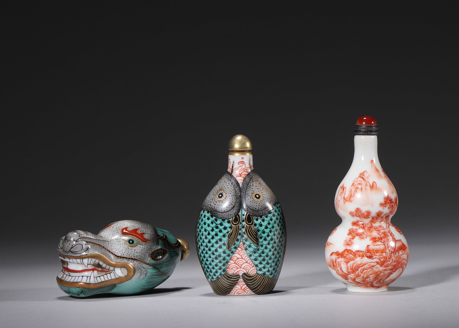 A SET OF THREE FAMILLE-ROSE PORCELAIN SNUFF BOTTLES: A set of three porcelain snuff bottles in beast-head, twin-fish and double-gourd forms, decorated in famille rose, ink and iron red with landscape motifs and gilt highlights. The bases bear marks