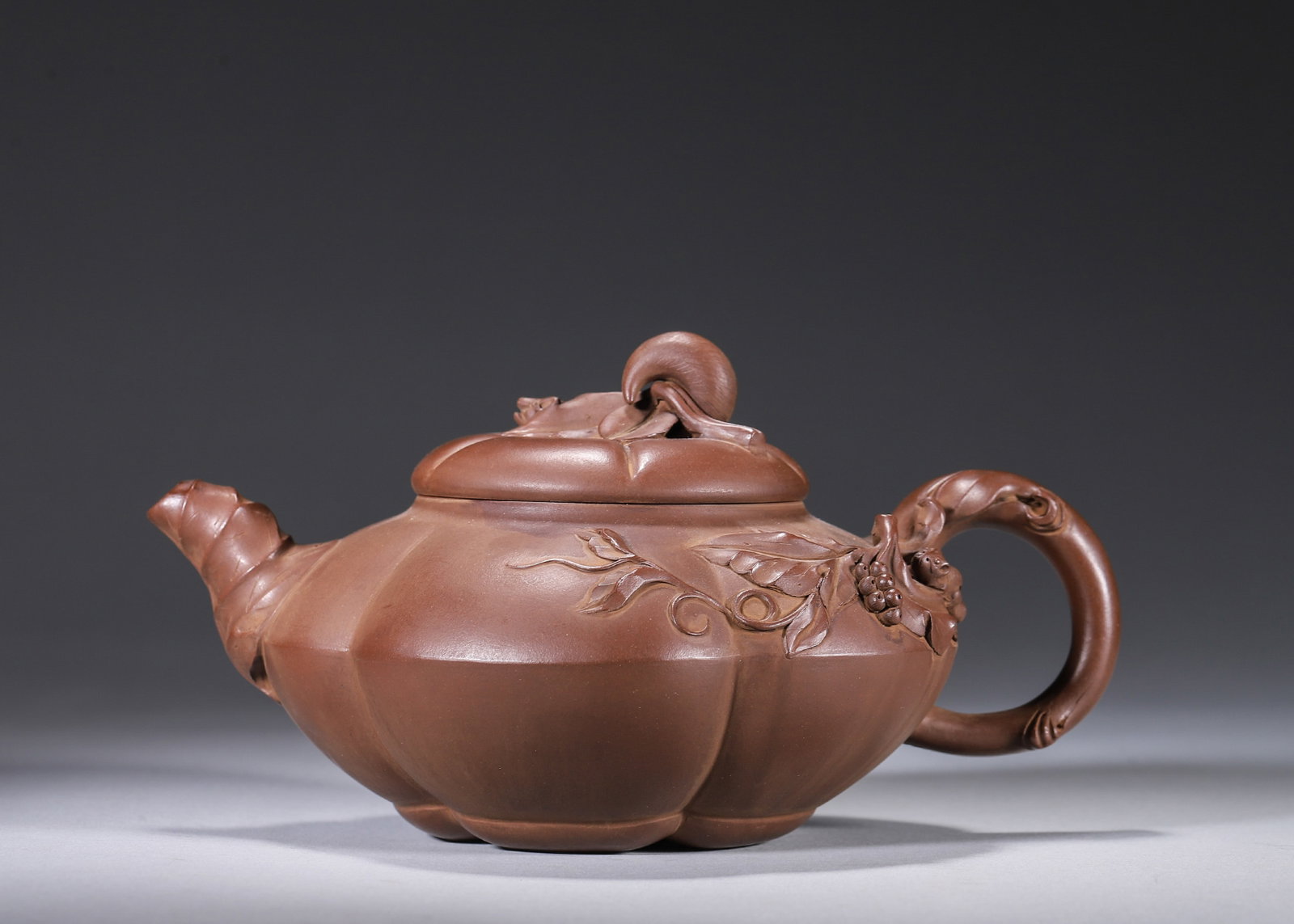 A ZISHA 'SQUIRREL AND GRAPE' MELON-FORM TEAPOT: A zisha teapot of melon-lobed form, decorated with molded squirrels and grape vines. The base bears a seal in the name of Xie Manlun. L. 19 cm; W. 14 cm; Ht. 9 cm.