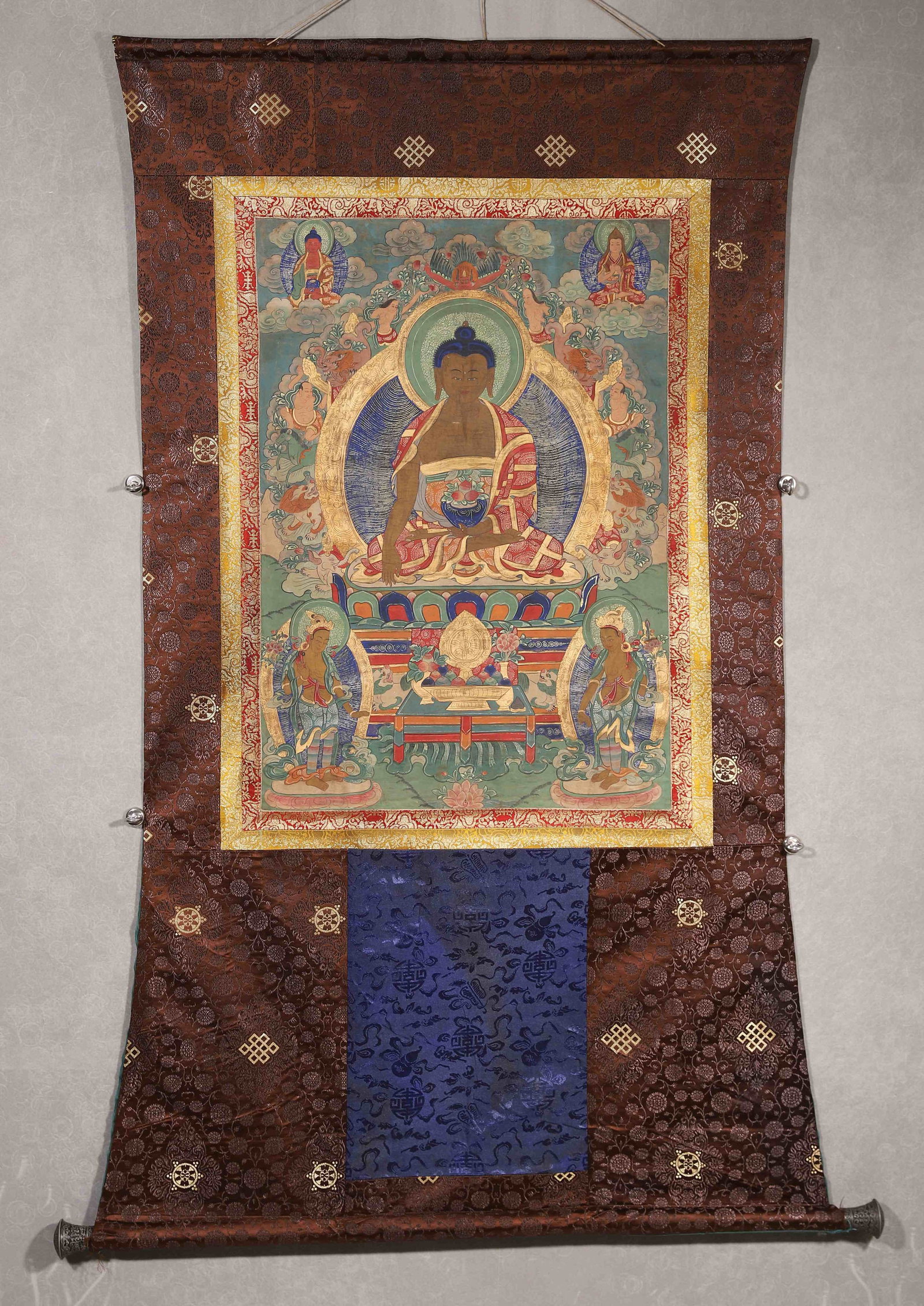 A THANGKA OF SHAKYAMUNI BUDDHA: A mineral-pigment thangka depicting Shakyamuni Buddha seated in lotus posture, the right hand in earth-touching mudra and the left holding an alms bowl, with Amitabha Buddha, Tsongkhapa, attendants, c