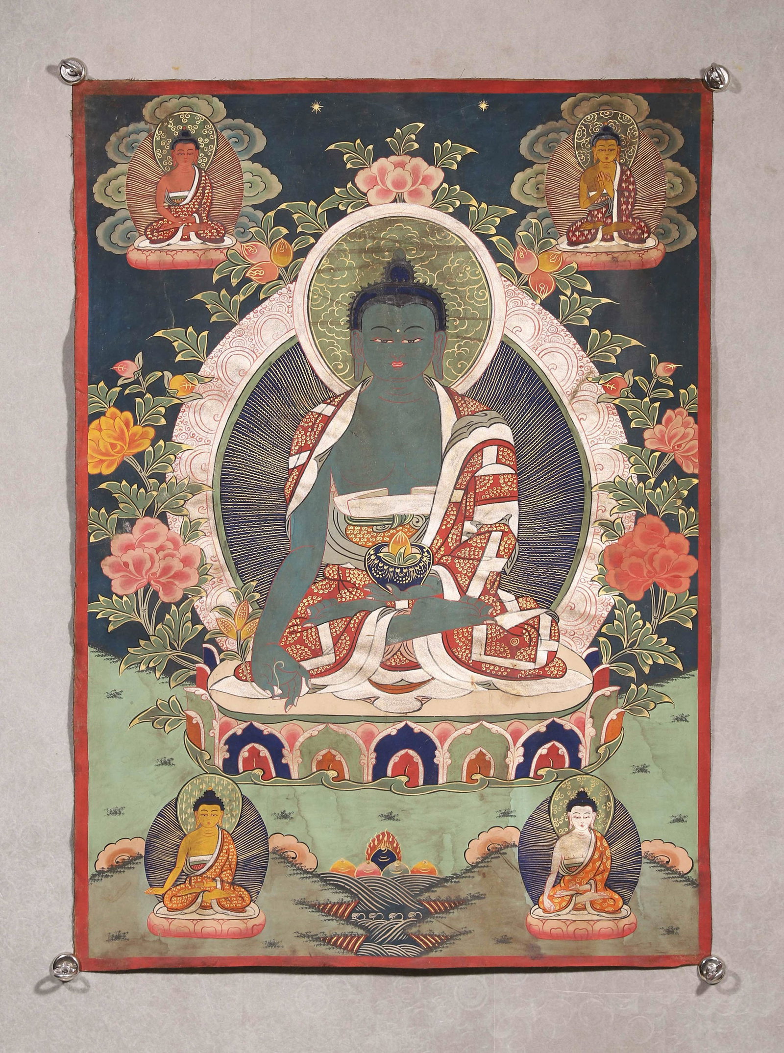 A THANGKA OF BHAISAJYAGURU: A mineral-pigment thangka depicting Bhaisajyaguru seated in lotus posture, the right hand in varada mudra and the left holding a medicine bowl with medicinal fruit, surrounded by four attendant Buddha