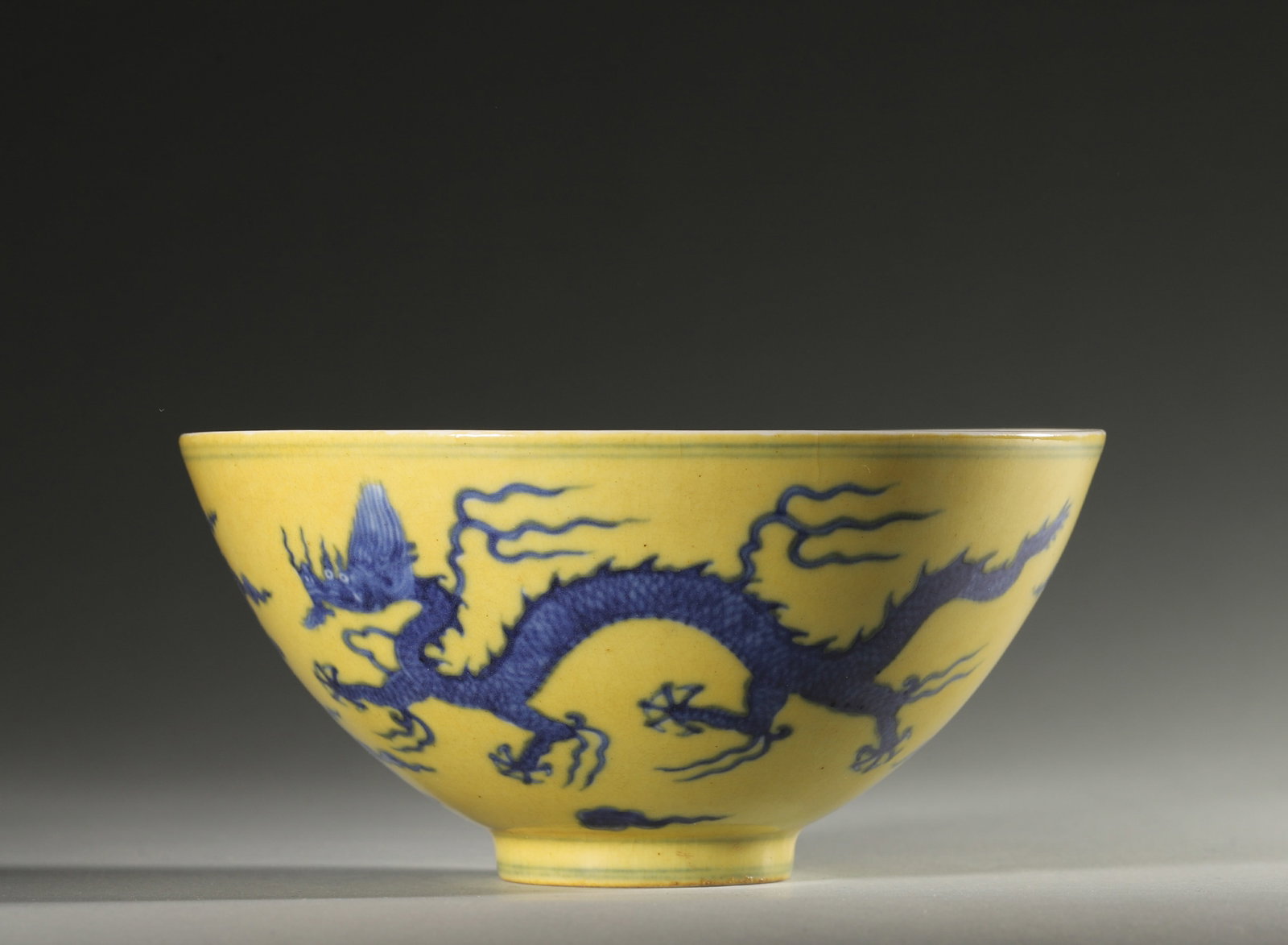 A YELLOW-GROUND BLUE-AND-WHITE 'DRAGON AND CLOUD' BOWL: A porcelain bowl with a yellow ground, decorated in underglaze blue with a dragon amid clouds, with a plain white interior. The base bears a mark described in the source as Hongzhi. Diam. 16.5 cm; Ht.