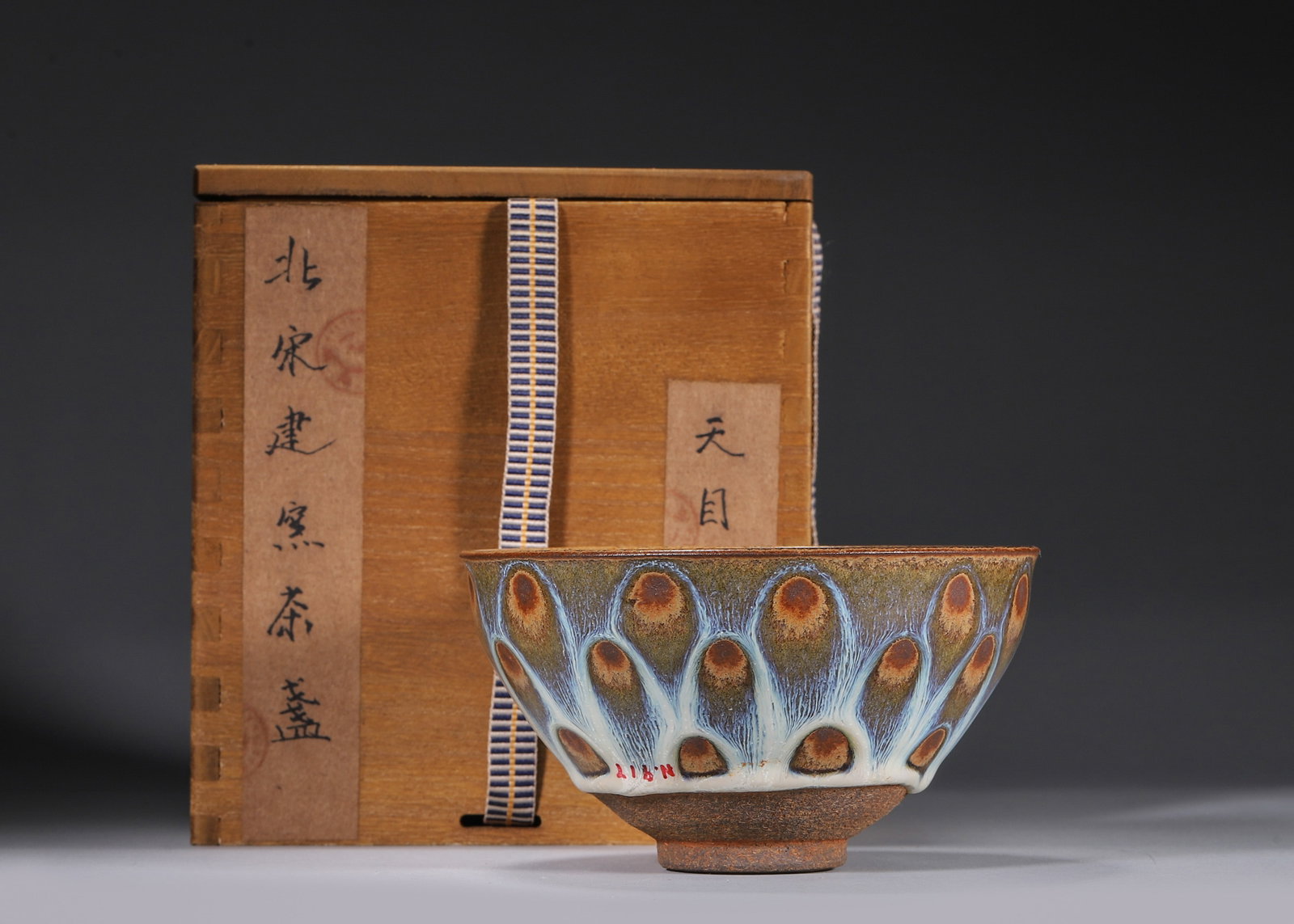A 'PEACOCK-EYE' JIAN-STYLE TEA BOWL: A Jian-style tea bowl covered in a dark glaze with pale blue-white peacock-eye spots and streaks. The base bears a two-character incised mark reading 'Gong Yu'. Diam. 13 cm; Ht. 7.5 cm. Note: With a b