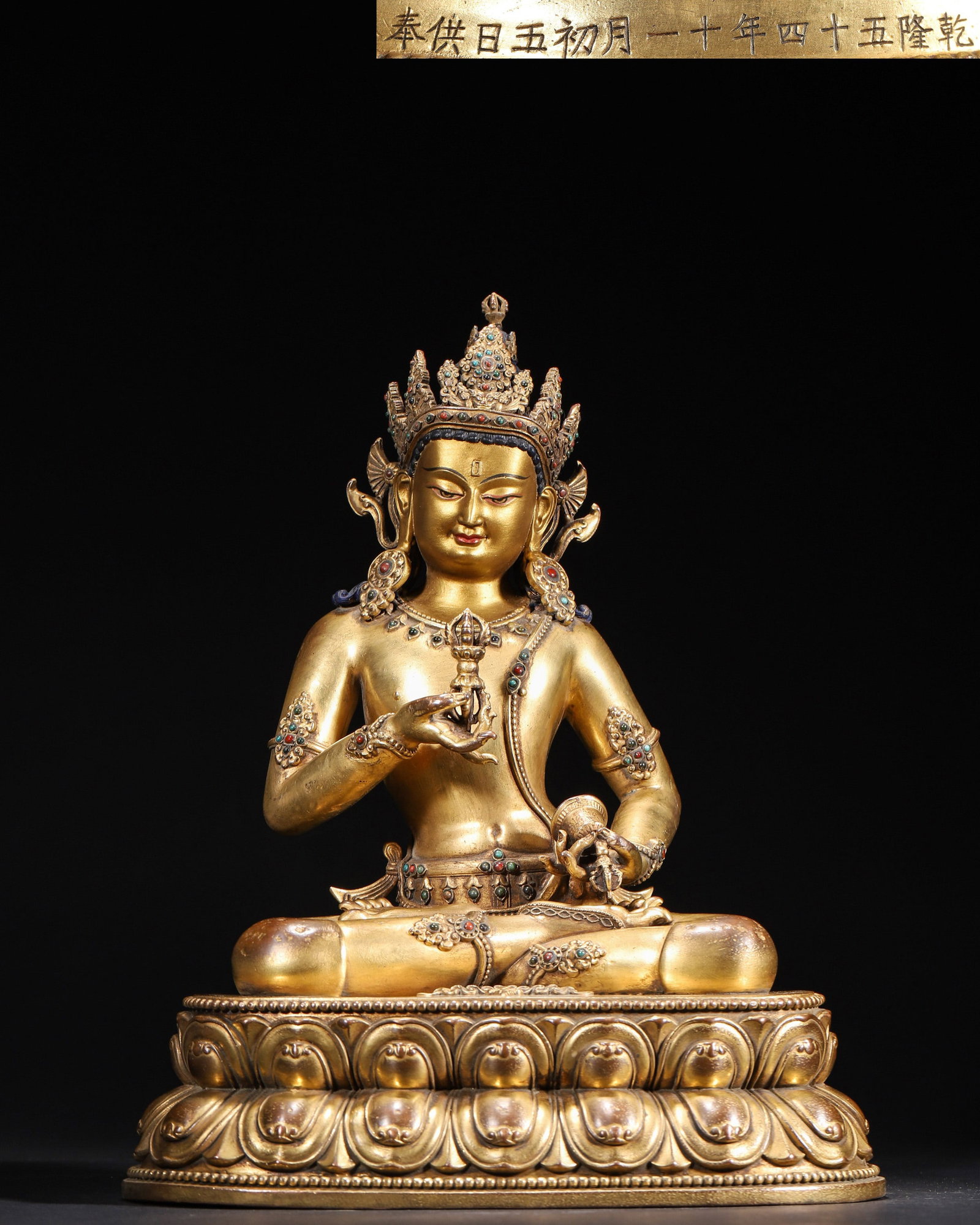 A GILT-BRONZE FIGURE OF VAJRASATTVA WITH COLORED-STONE INLAY: A gilt-bronze figure of Vajrasattva seated on a lotus base and set with colored stones. The base bears a dated inscription including 'Qianlong 54th Year'. Dimensions: 25 x 18 x 31 cm; Wt. 3,991 g.