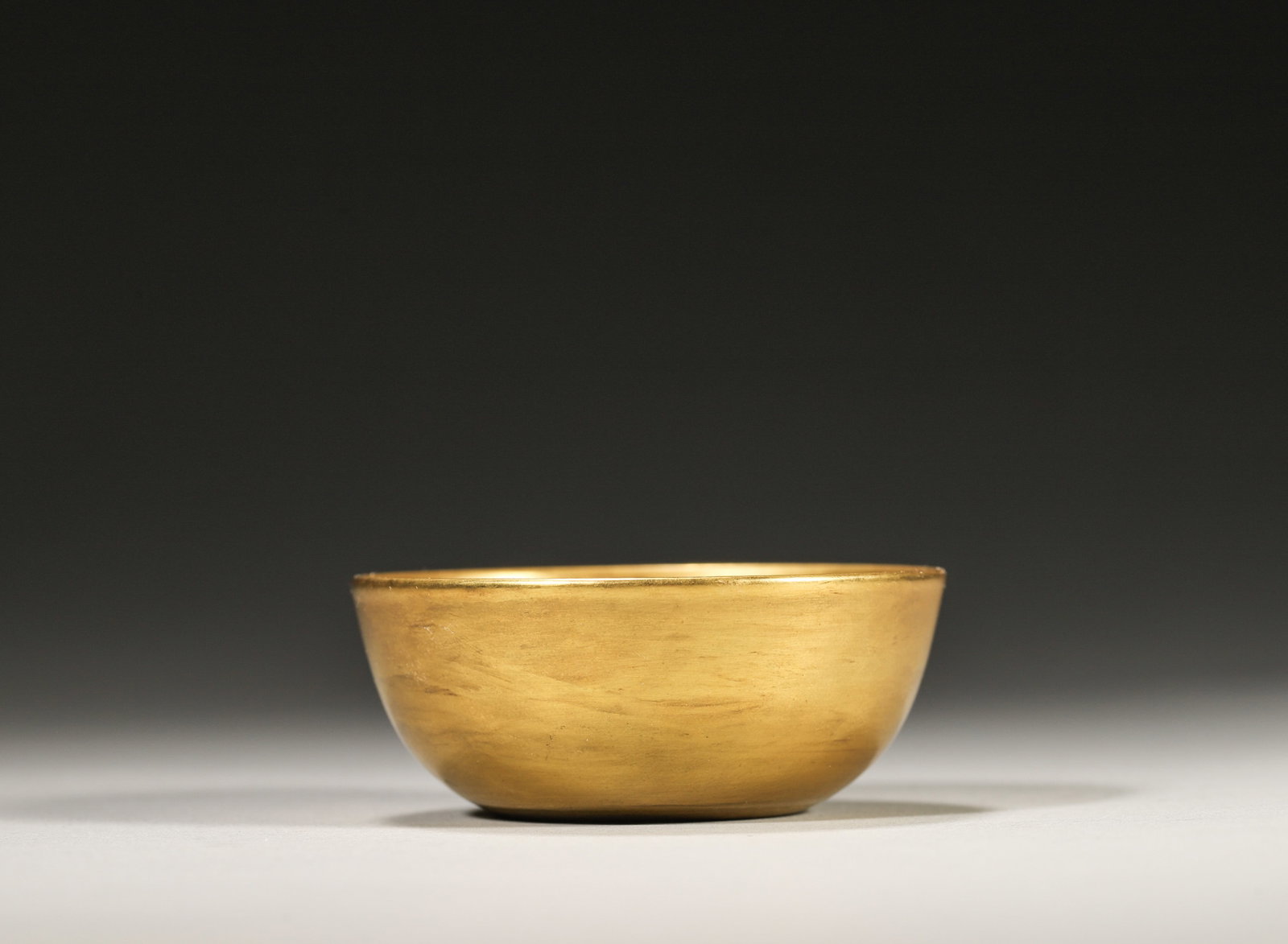 A GILT-GLAZED PORCELAIN BOWL: A porcelain bowl covered in a gilt glaze. The base bears a mark described in the source as Yongzheng. Diam. 5.8 cm; Ht. 2.5 cm.