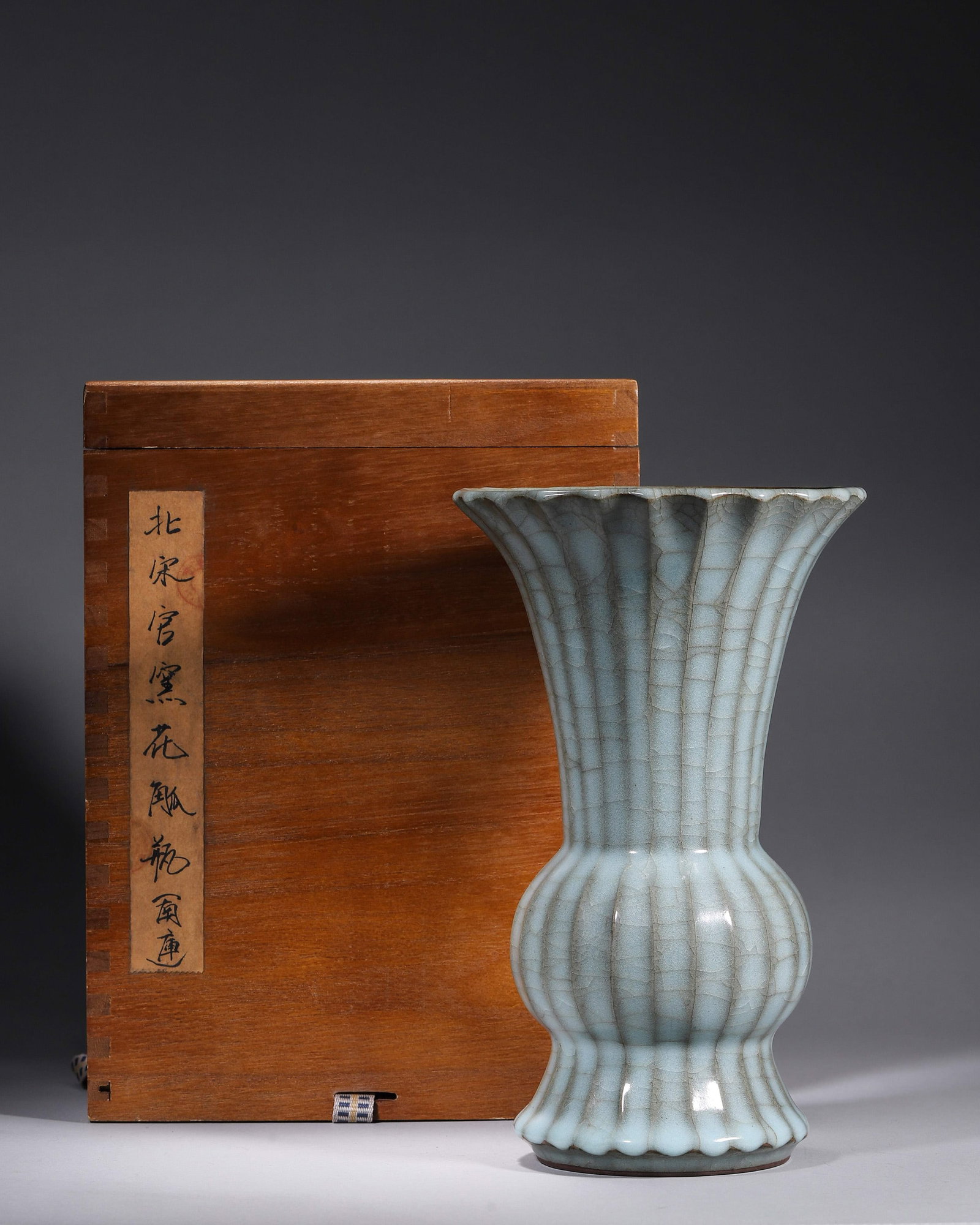 A GUAN-TYPE CELADON CHRYSANTHEMUM-FORM GU VASE: A chrysanthemum-ribbed gu-form porcelain vase with flared rim and slender neck, covered in a sky-blue Guan-type crackle glaze. Diam. 15 cm; Ht. 24 cm. Note: With a box and labels.