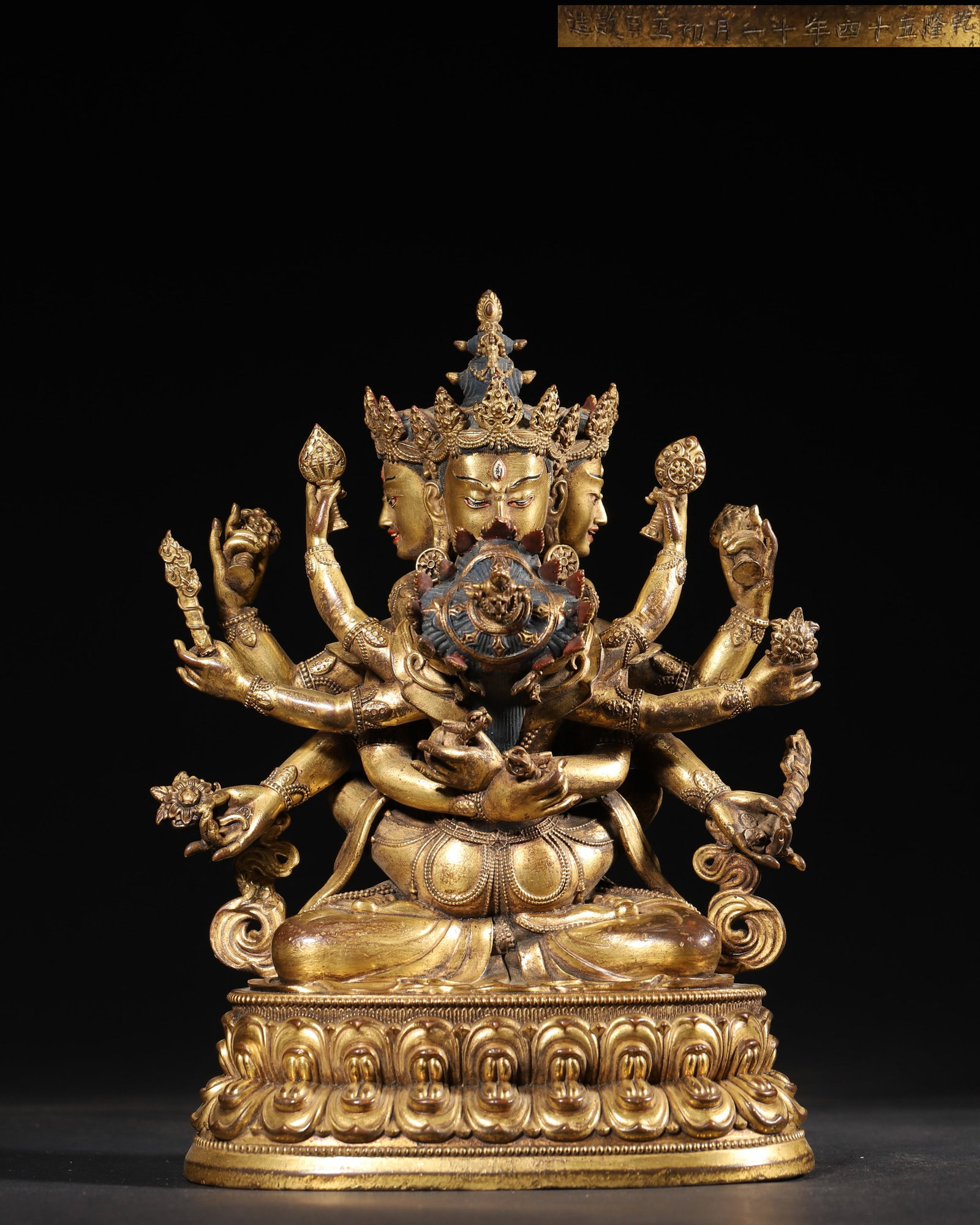 A GILT-BRONZE FIGURE OF GUHYASAMAJA: A gilt-bronze figure of Guhyasamaja seated on a lotus base. The base bears an inscription and a crossed-vajra motif. Dimensions: 16 x 13 x 23 cm; Wt. 3,155 g.