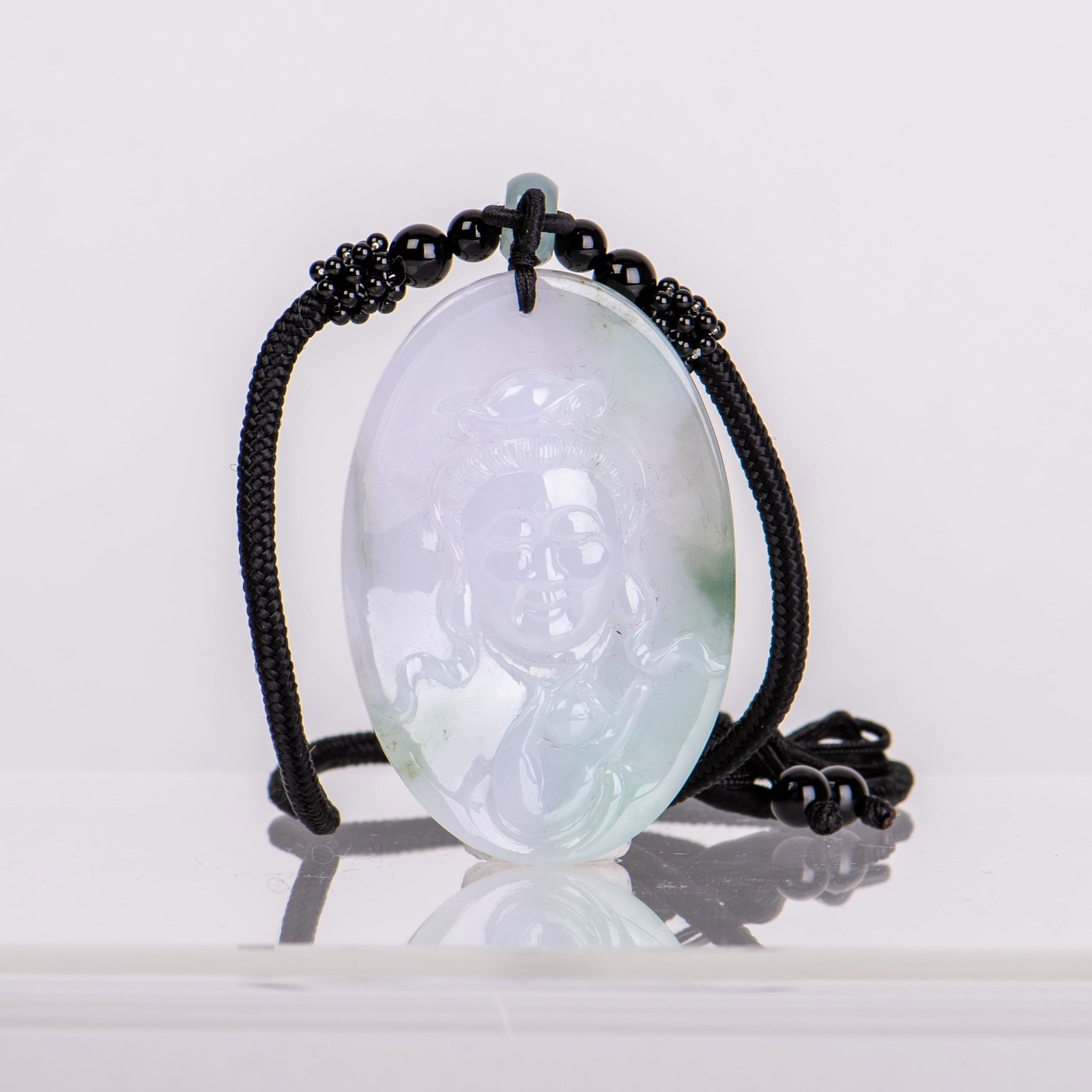 A JADEITE PENDANT CARVED WITH GUANYIN: A jadeite pendant carved with Guanyin, the smoothly polished stone of a pale green tone. 2.25"h x 0.25"w x 1.5"l (5.72 x 0.64 x 3.81 cm)