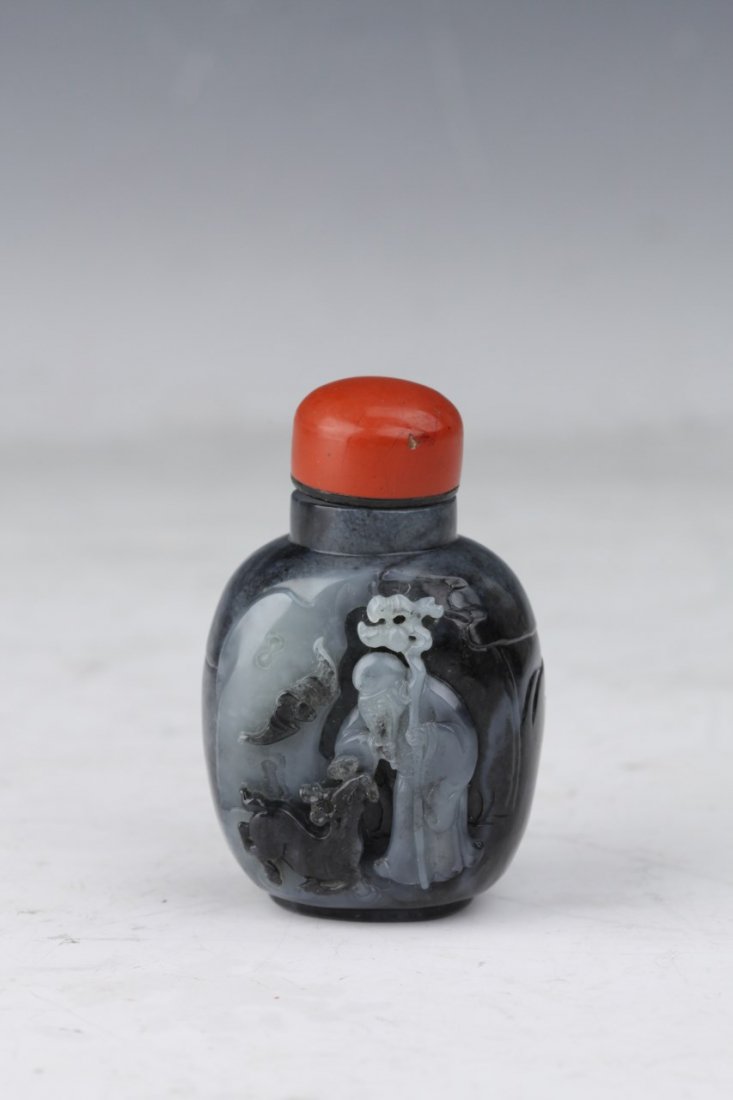 An Unusual White Chinese Jade Snuff Bottle: Charcoal grey Chinese Jade snuff bottle with light grey and white suffusions featuring a wise deity holding a staff and petting a Pi Yao creature, with an agate cap. Height 3.5"