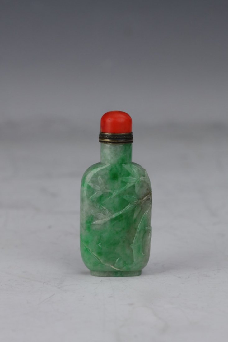 Jadeite Snuff Bottle: Nature green Jadeite snuff bottle of compressed cylindrical form with grey and white mottling featuring carved bamboo detailing and a gold and red cap. Height 3.25"