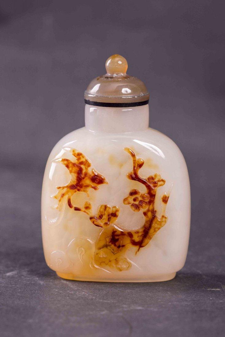 Chinese Agate Snuff Bottle: Chinese agate carved snuff bottle, with the design of a bird in mid flight and a flowering tree, of compressed form with recessed base and semi-precious stone cap. Length 2" Width 1" Height 2.75"